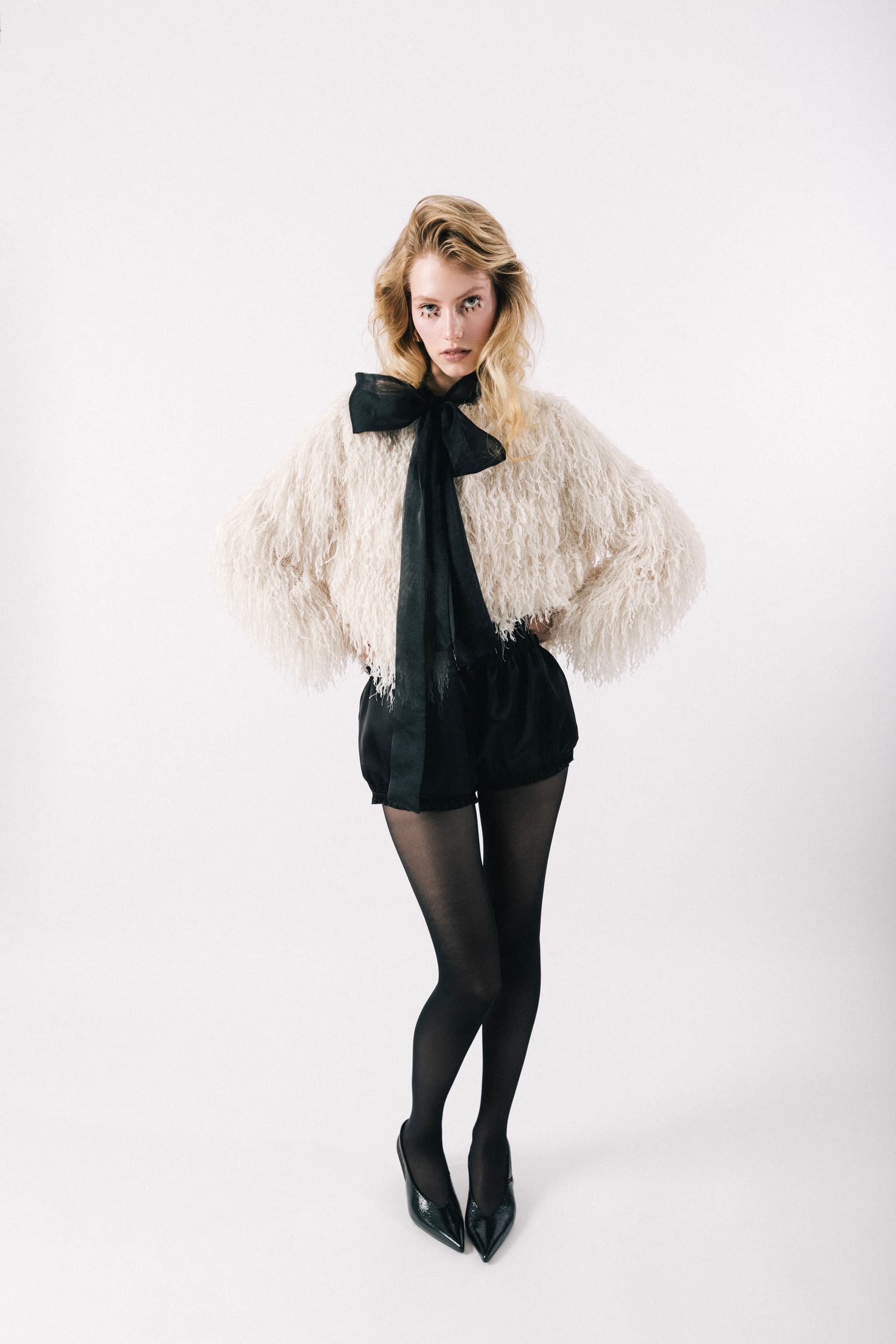 Fashionable woman in a chic fluffy top with a black bow, tights, and pointed heels.