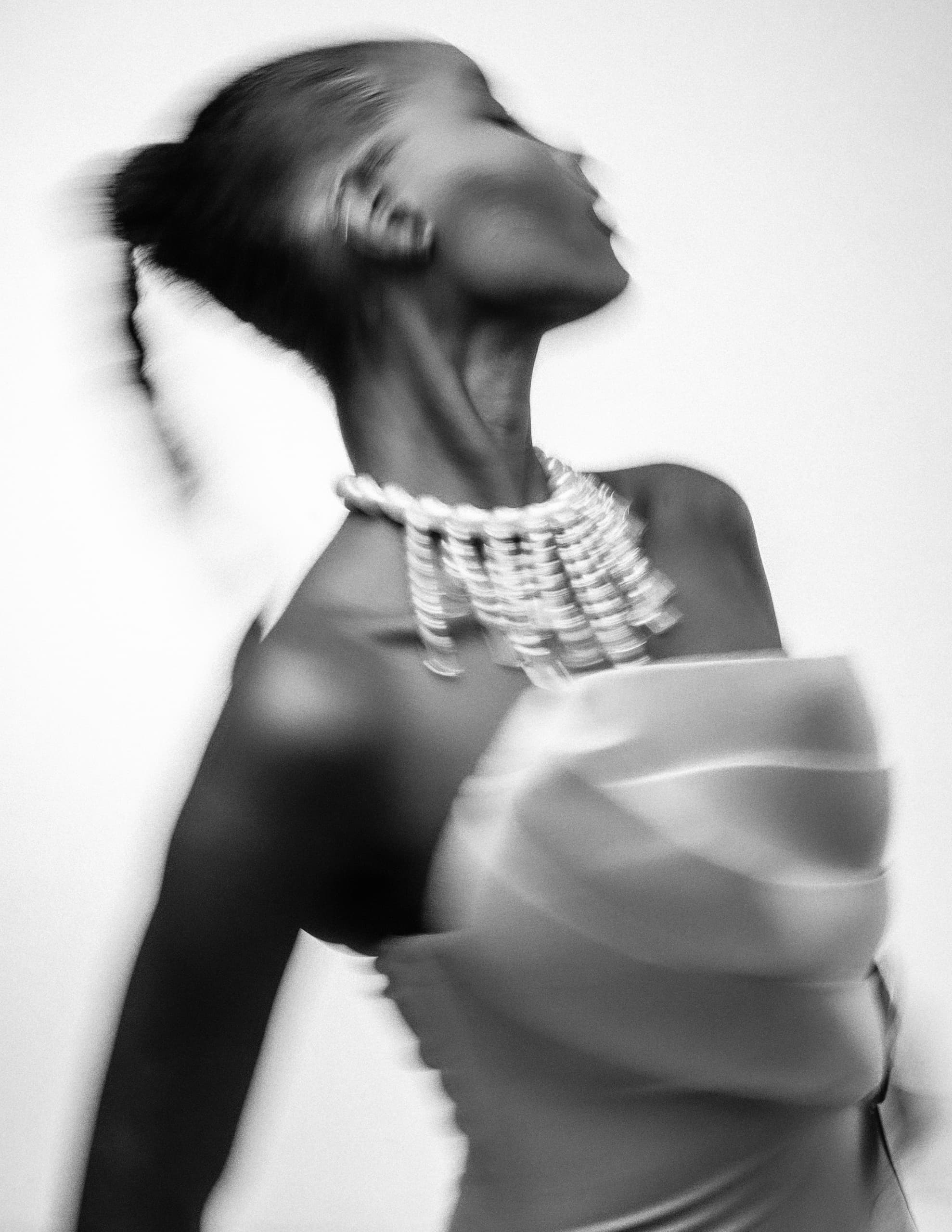 Blurry elegant woman in motion, wearing a layered dress and statement necklace.