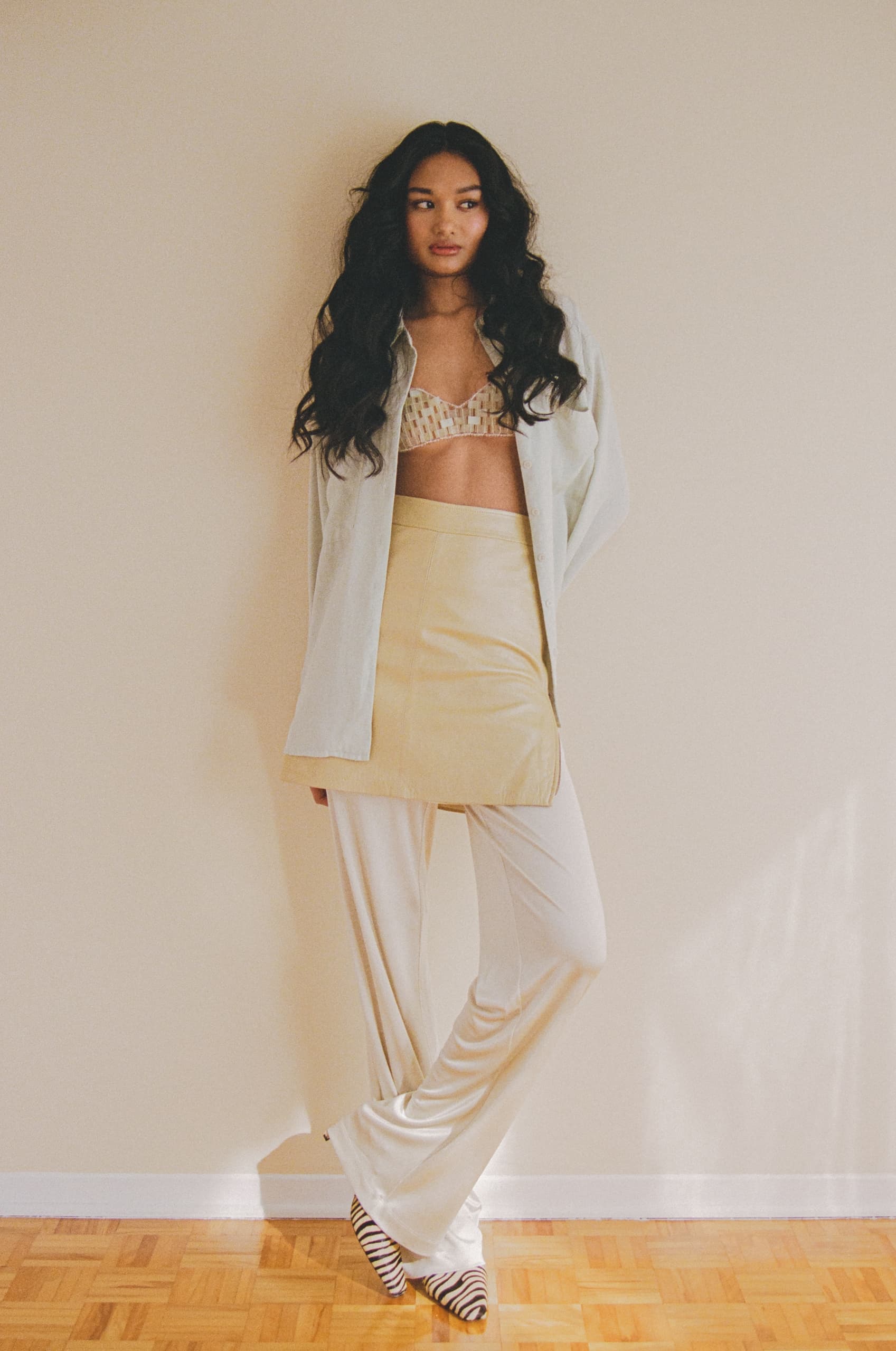 Woman in stylish layered outfit and zebra print shoes against a beige wall.