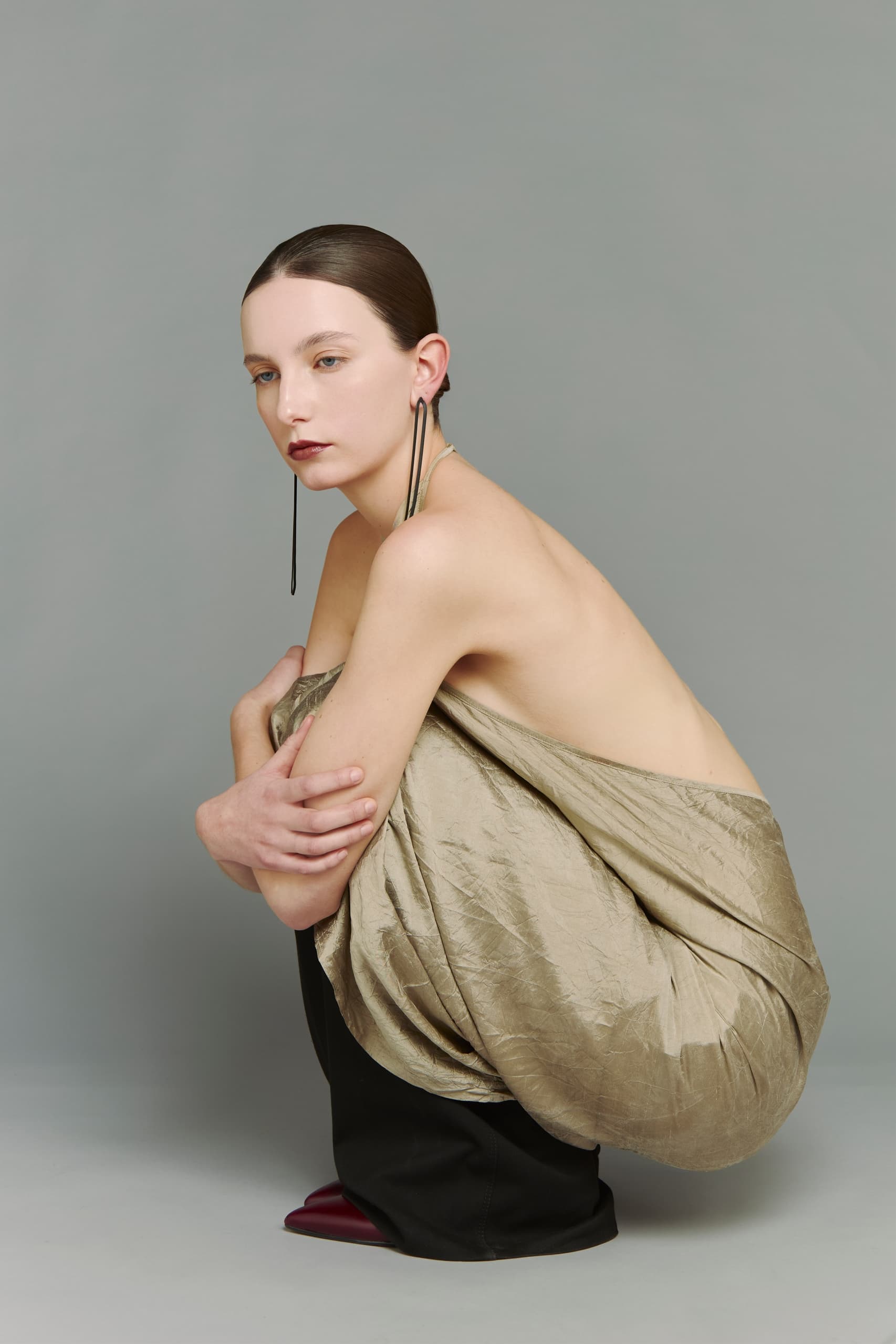 Fashion model in a unique fabric wrap with bold earrings, minimalist background.