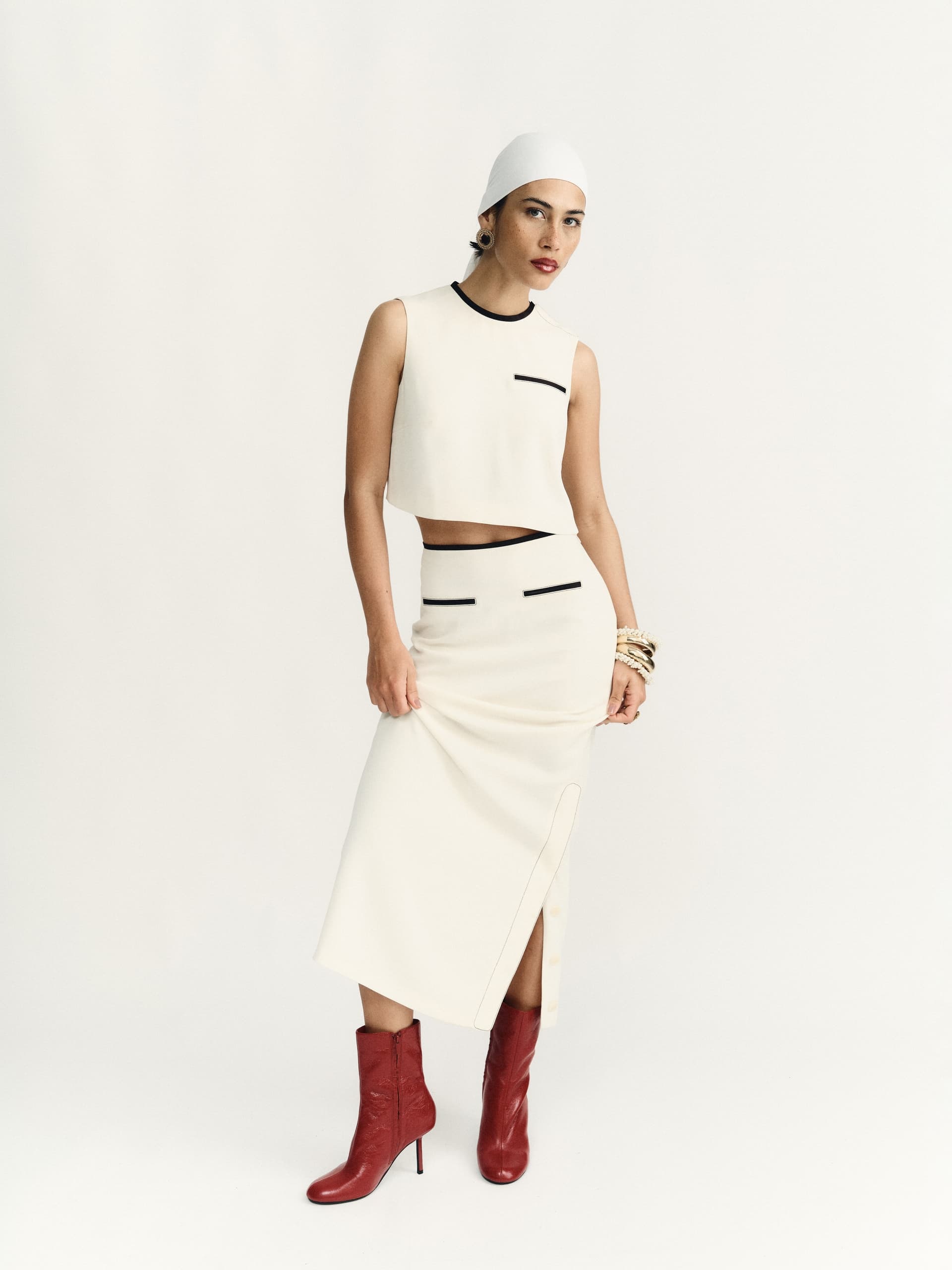 Elegant woman in chic white outfit with red boots and white headscarf.