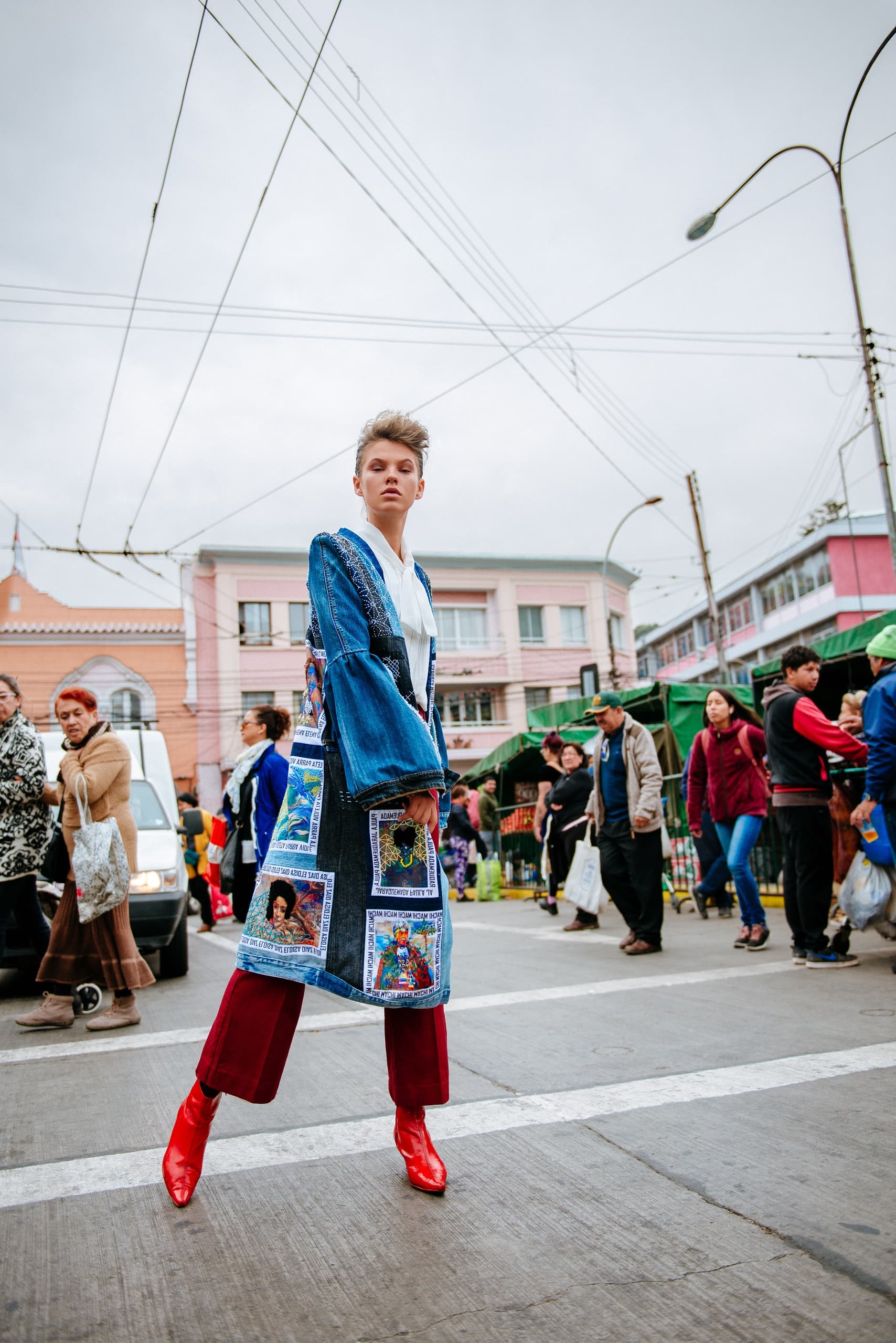 Fashionable person in denim coat and red boots on a lively city street.
