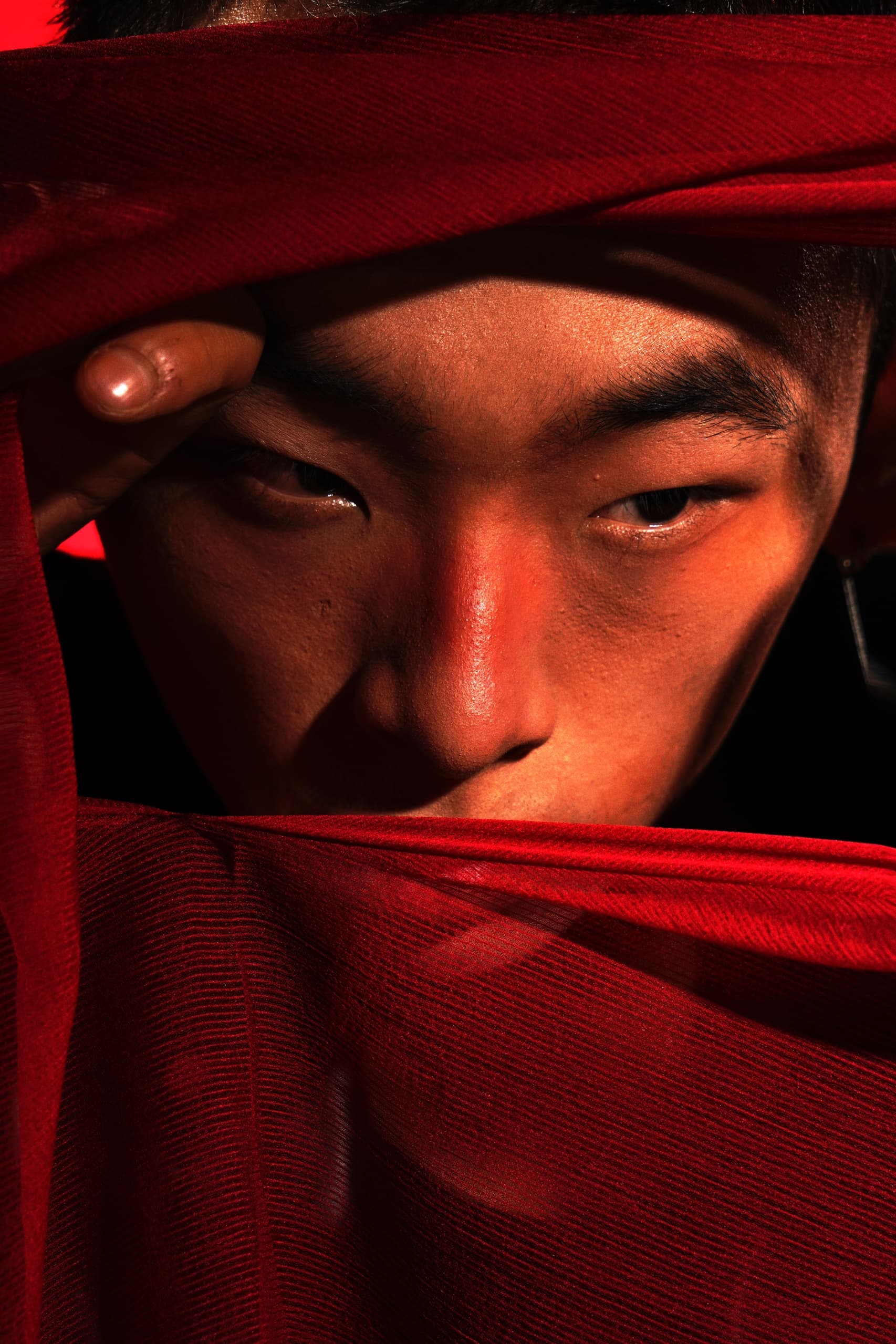 Mysterious man behind red fabric with intense gaze and dramatic lighting.