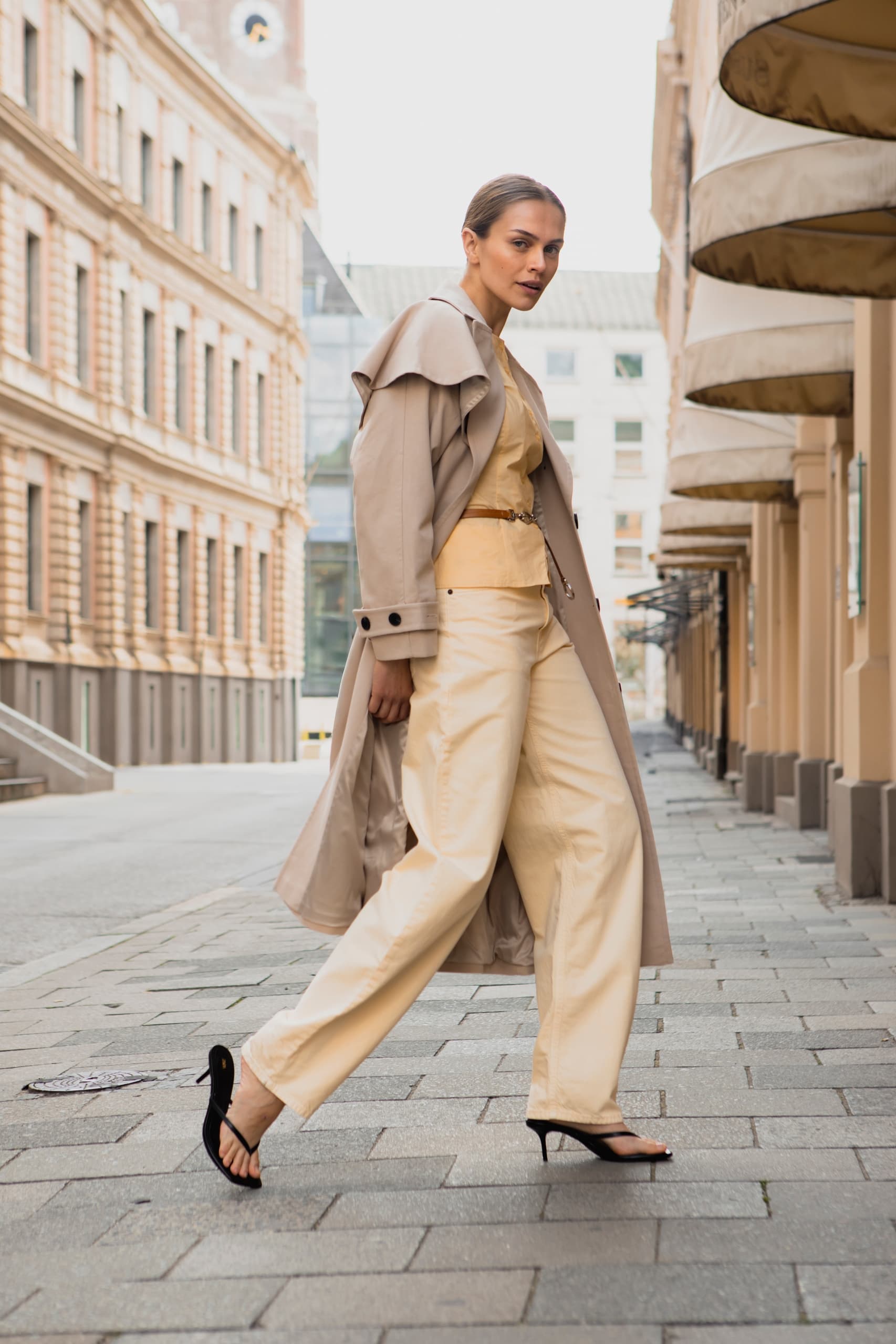 Fashionable woman in beige outfit and coat walking on a city street.