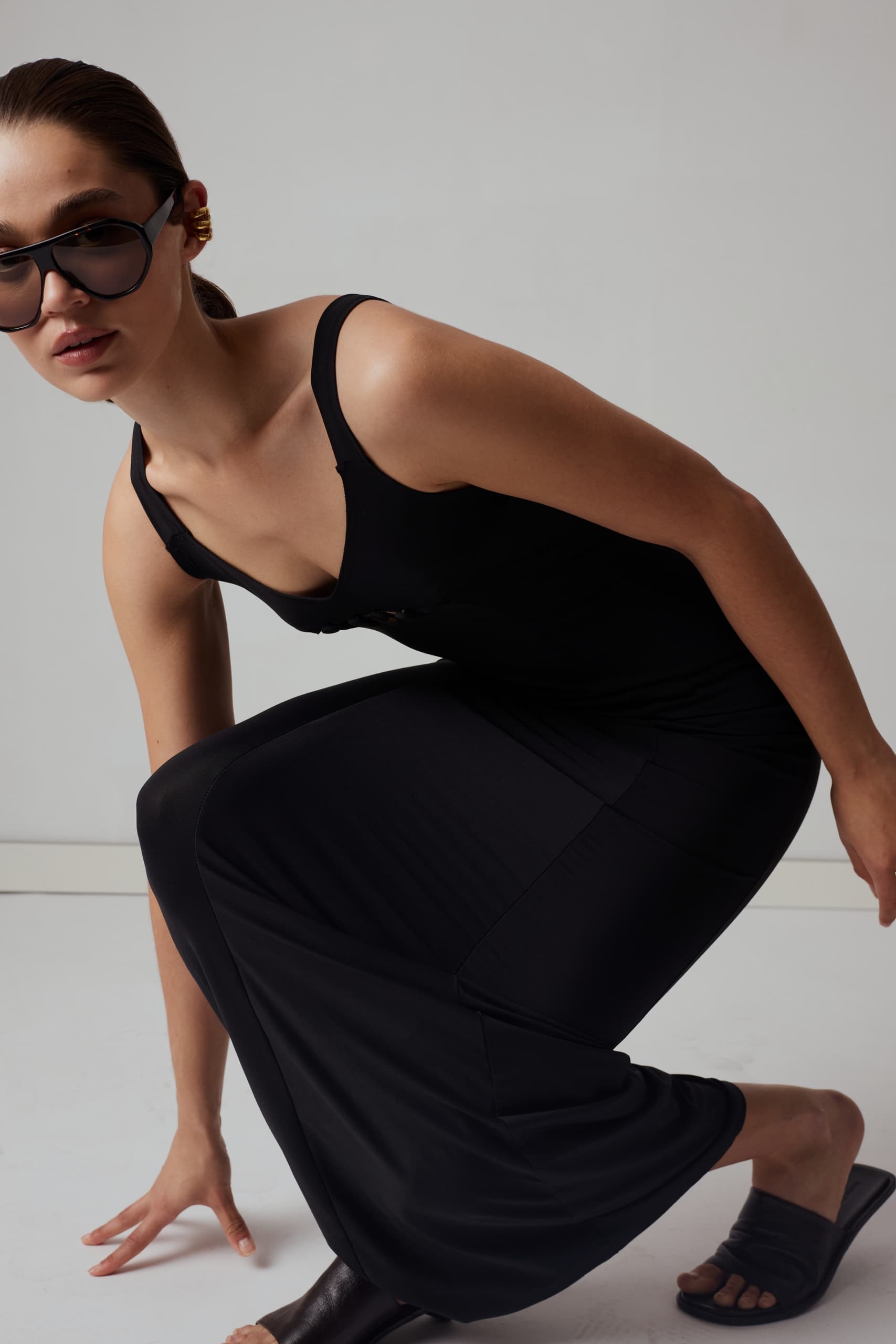 Fashionable woman in black dress and sunglasses crouching gracefully.