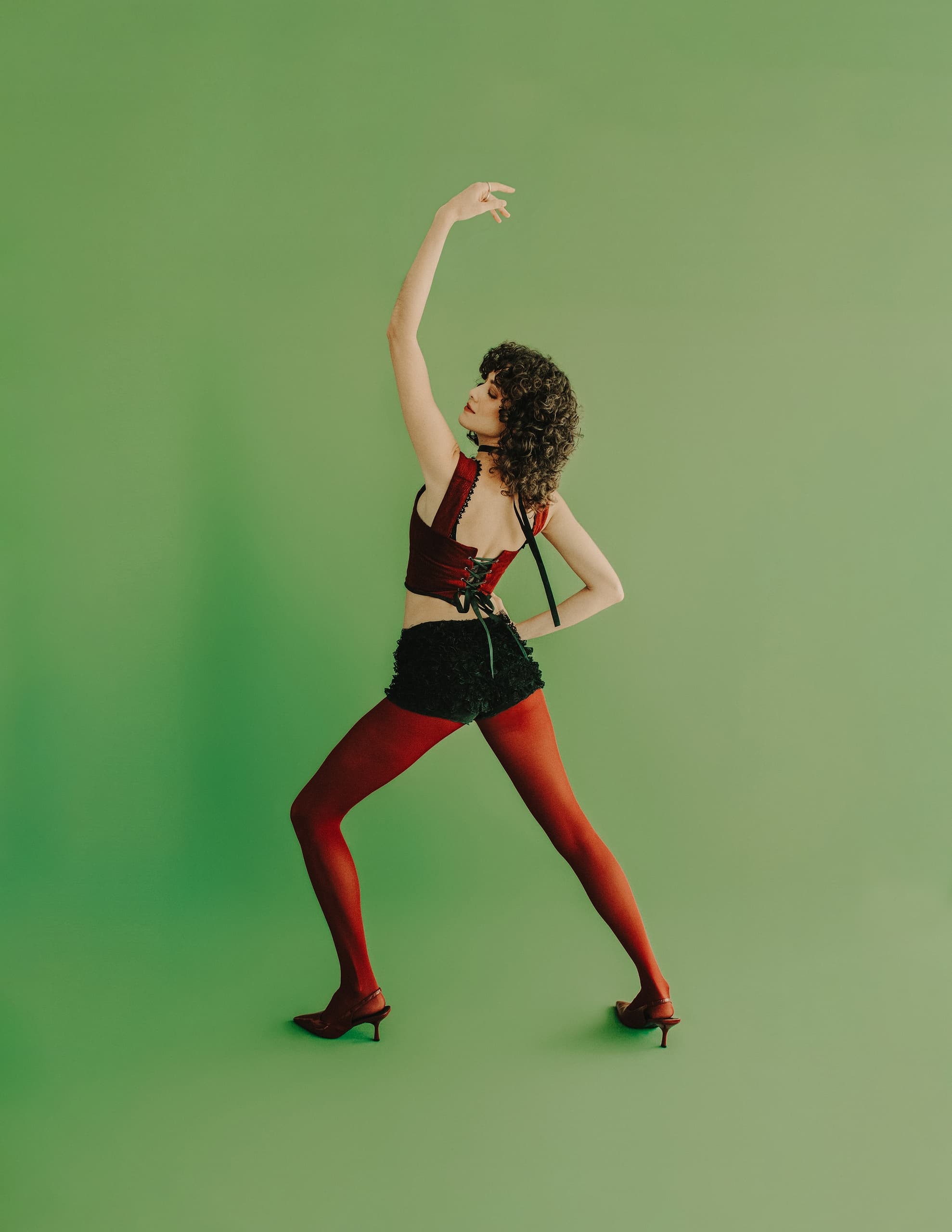 Person posing confidently in red outfit against a vibrant green background.