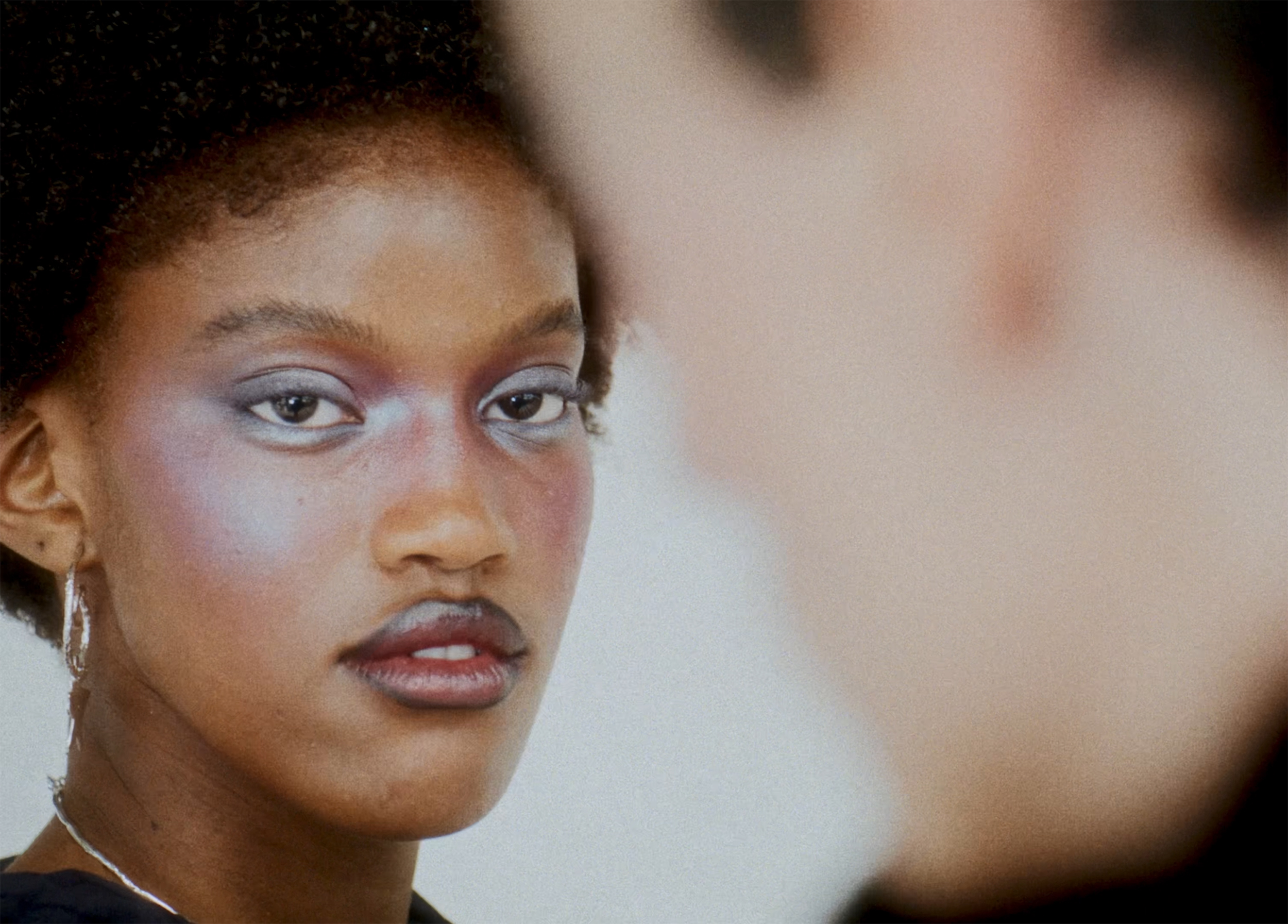 Woman with colorful makeup, intense gaze, facing person in soft focus.