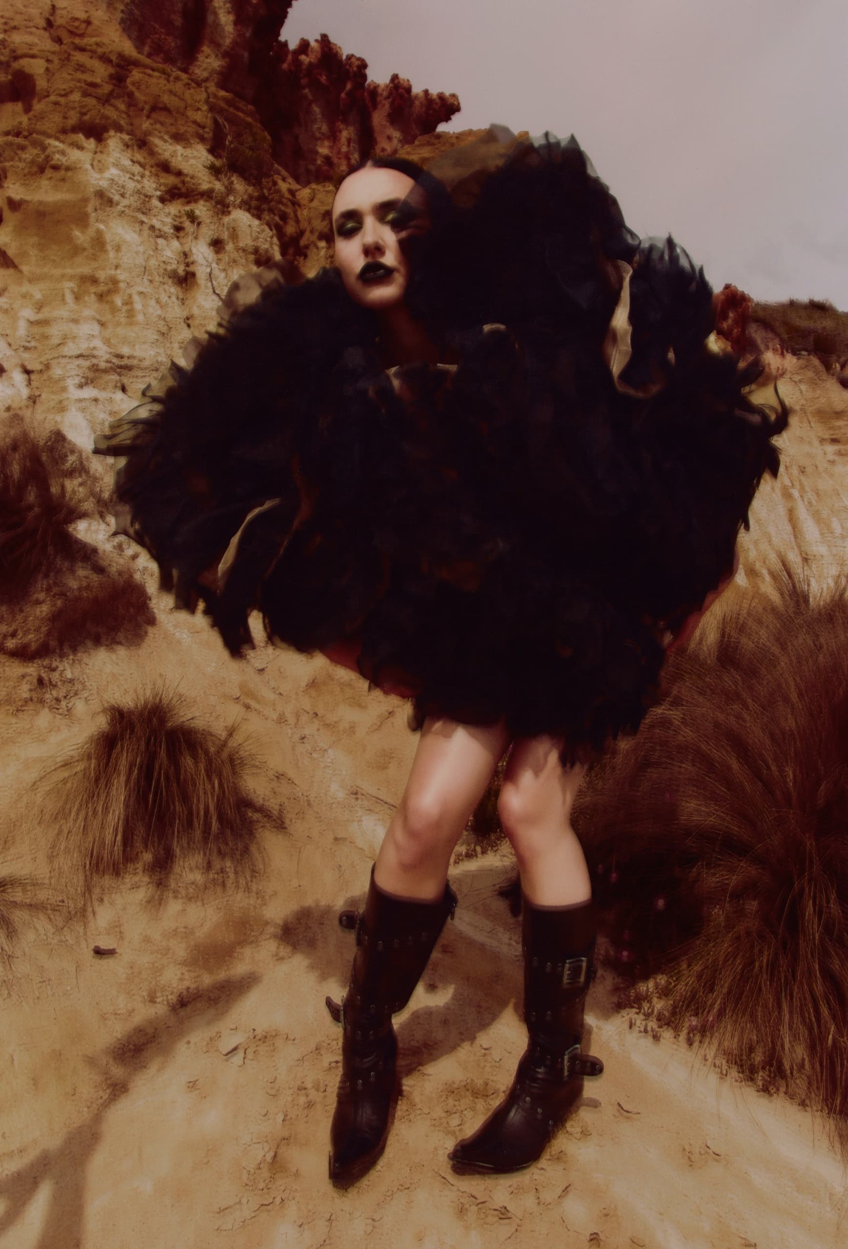 Person in high fashion attire with dark ruffles poses in a desert landscape.