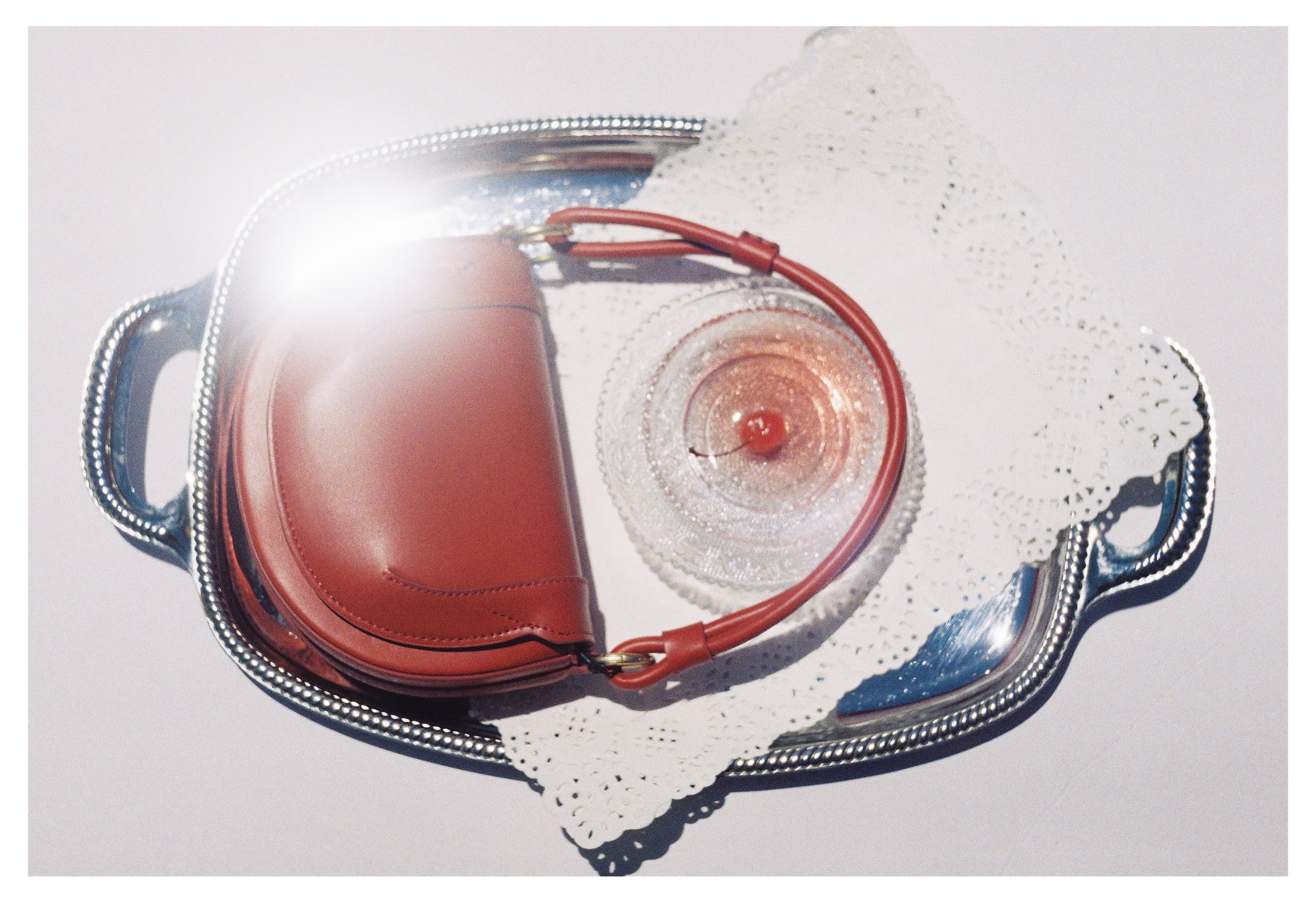 Red purse with cherry dessert on decorative silver tray.