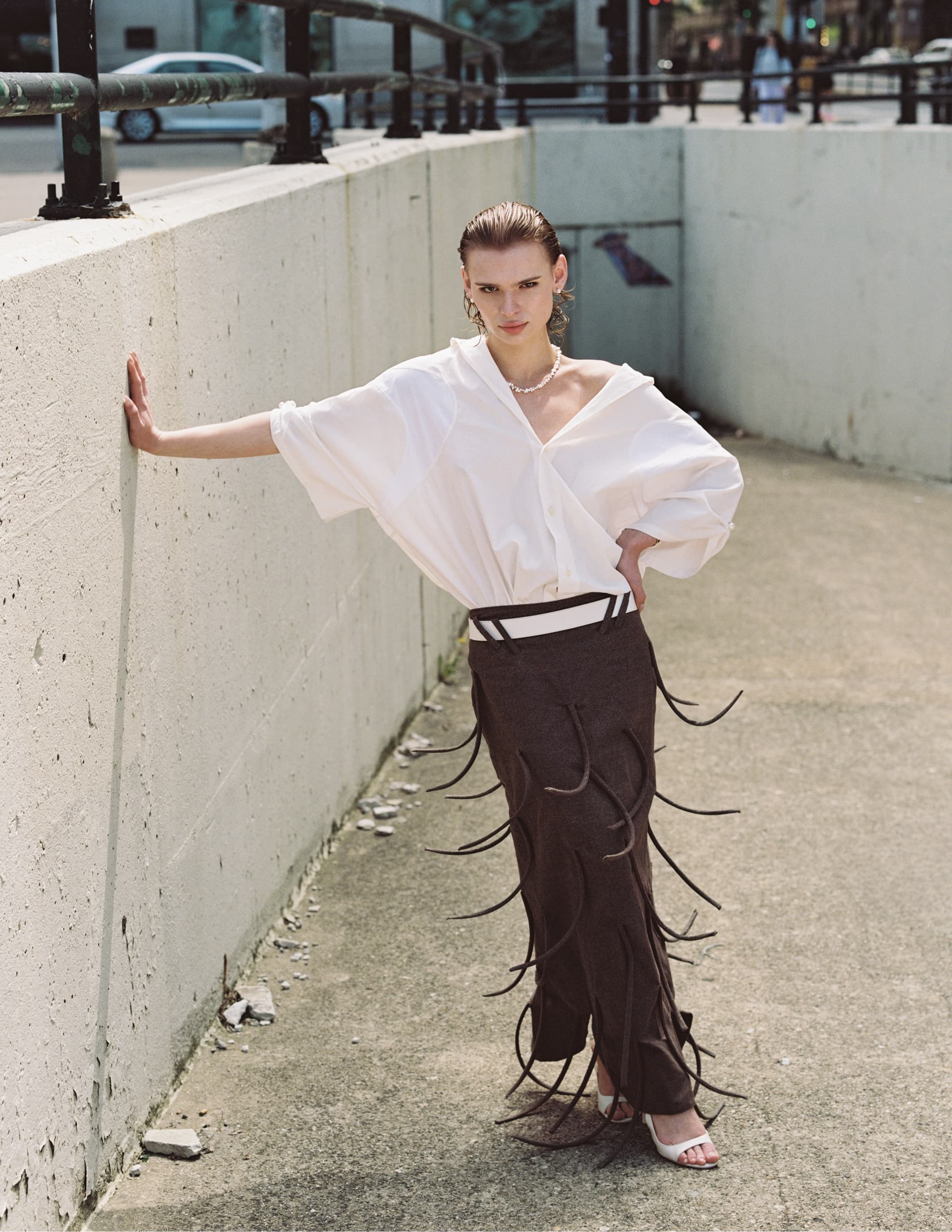 Stylish person in white shirt and unique skirt poses outdoors fashionably.