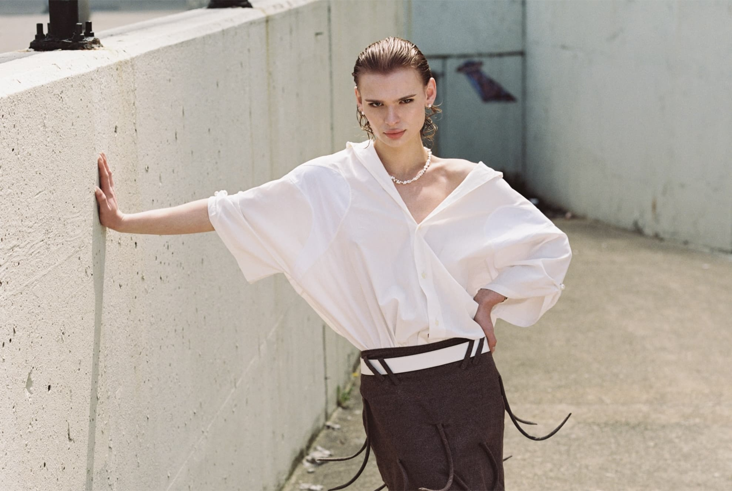 Fashionable woman poses in stylish outfit against a concrete wall.