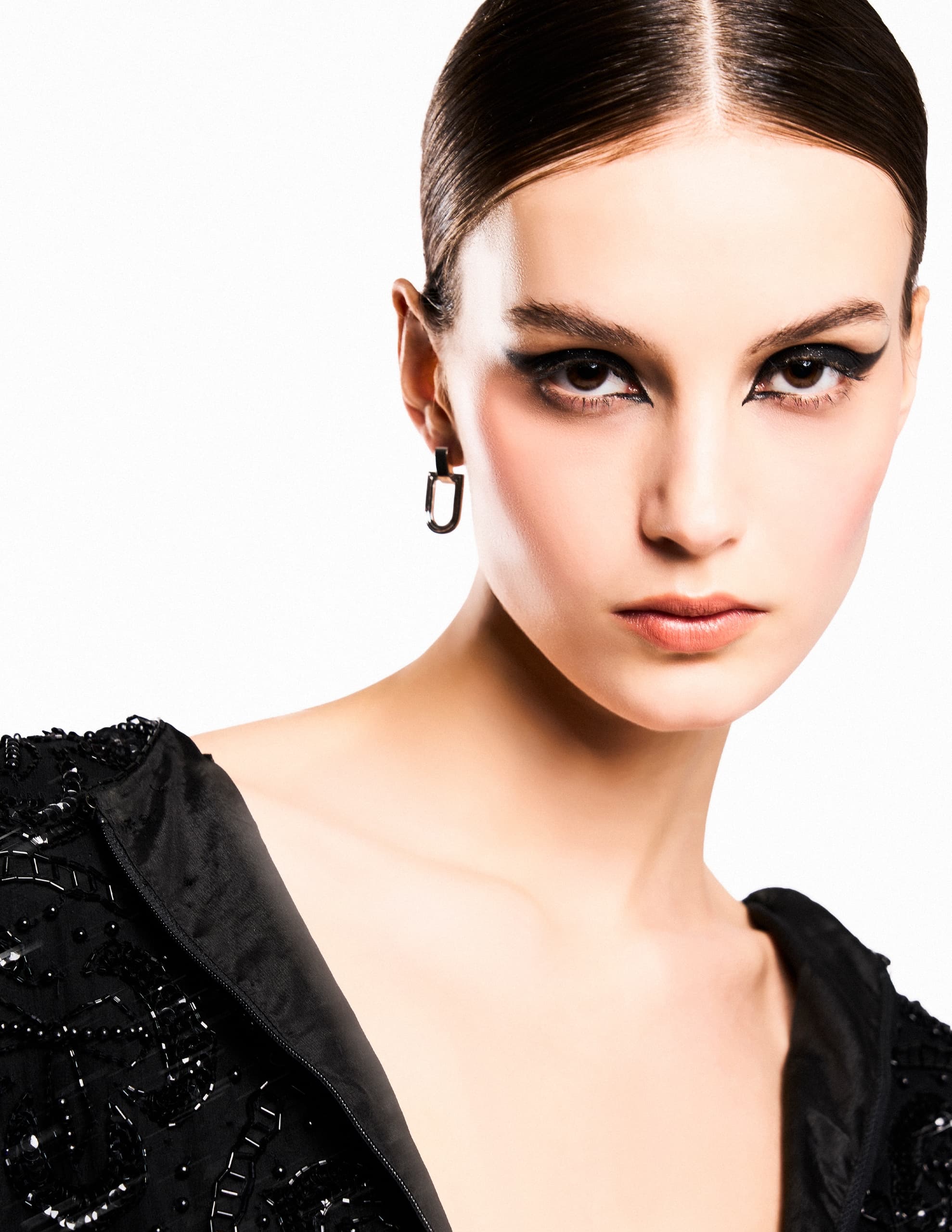 Elegant woman wearing bold makeup and black embellished outfit.