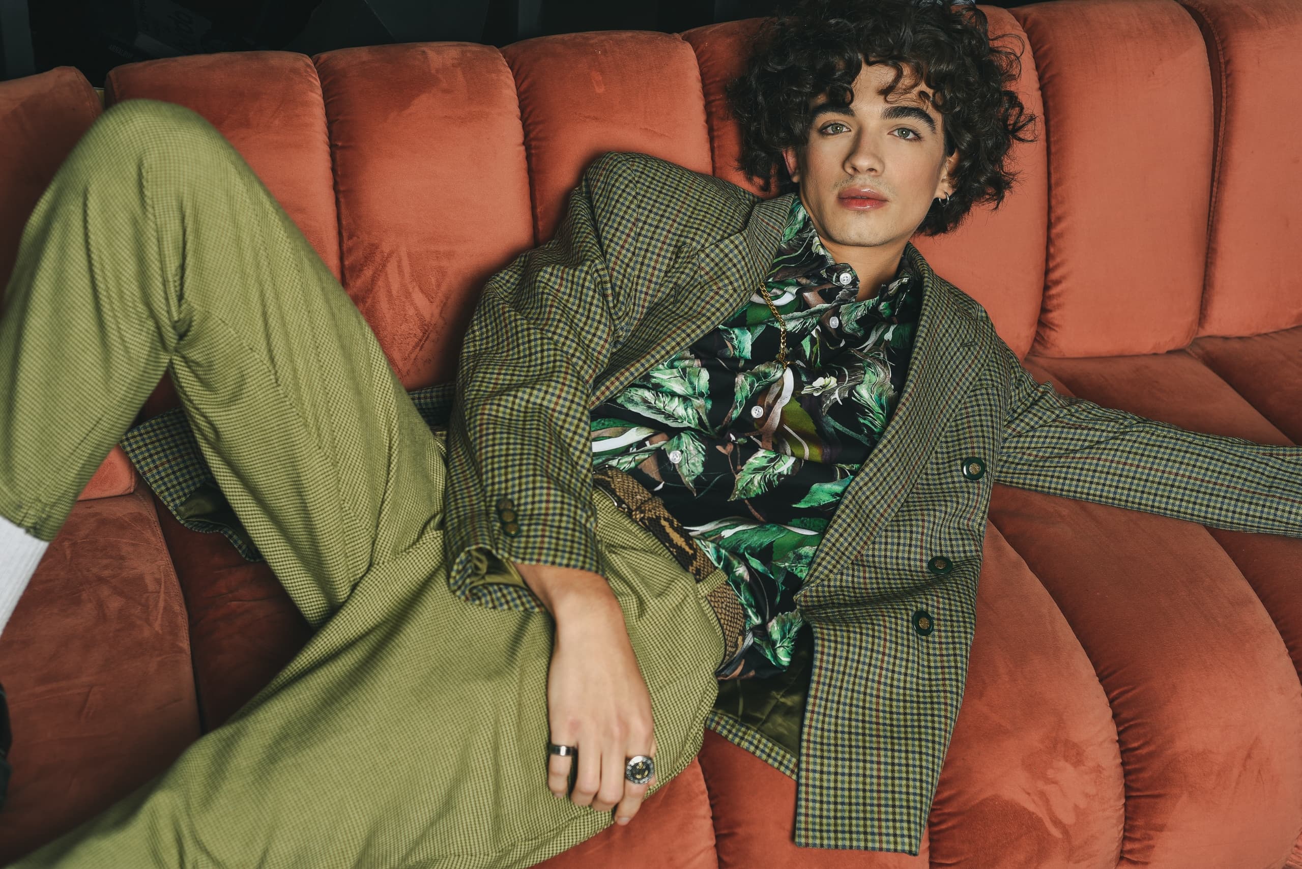 Fashionable person in green suit lounging on an orange sofa.