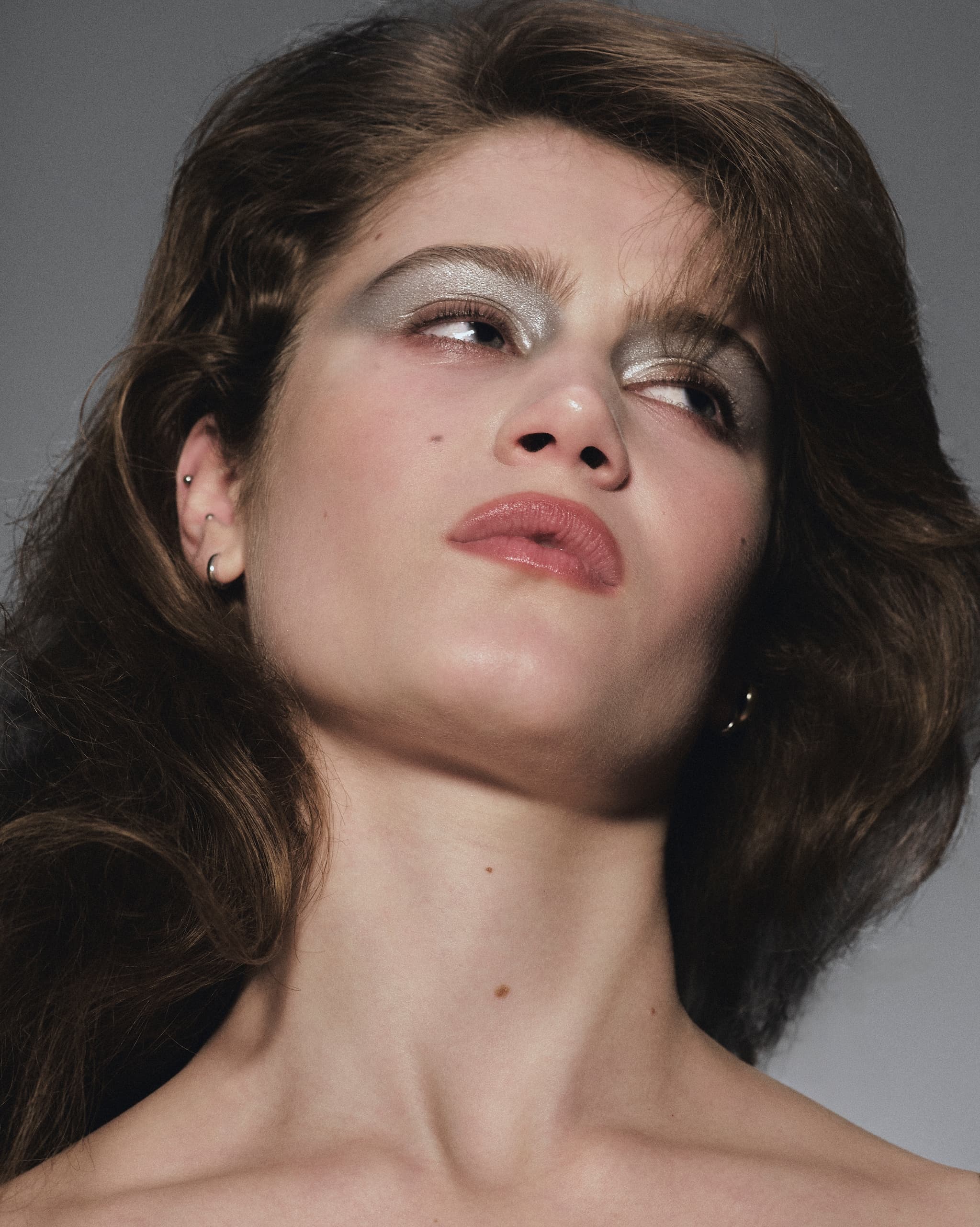 Woman with bold makeup and silver eyeshadow gazing upwards.