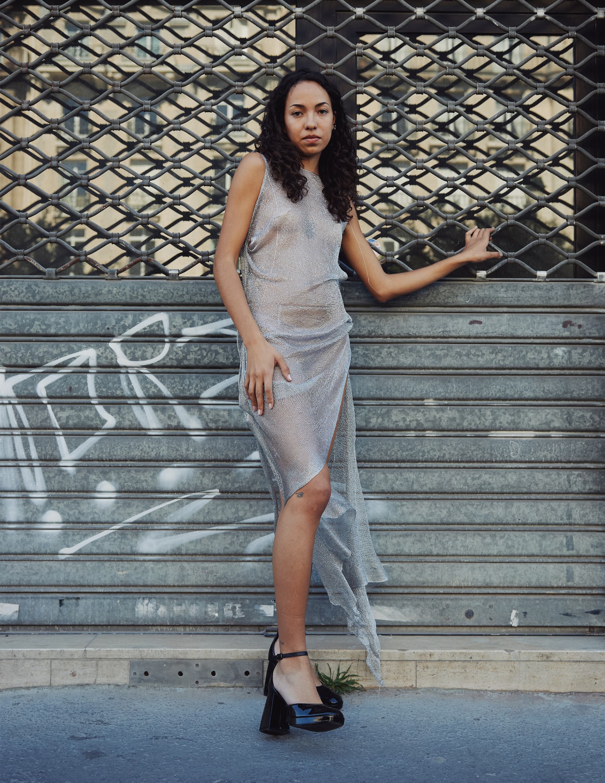 Woman posing in a stylish silver dress and black heels in an urban setting.