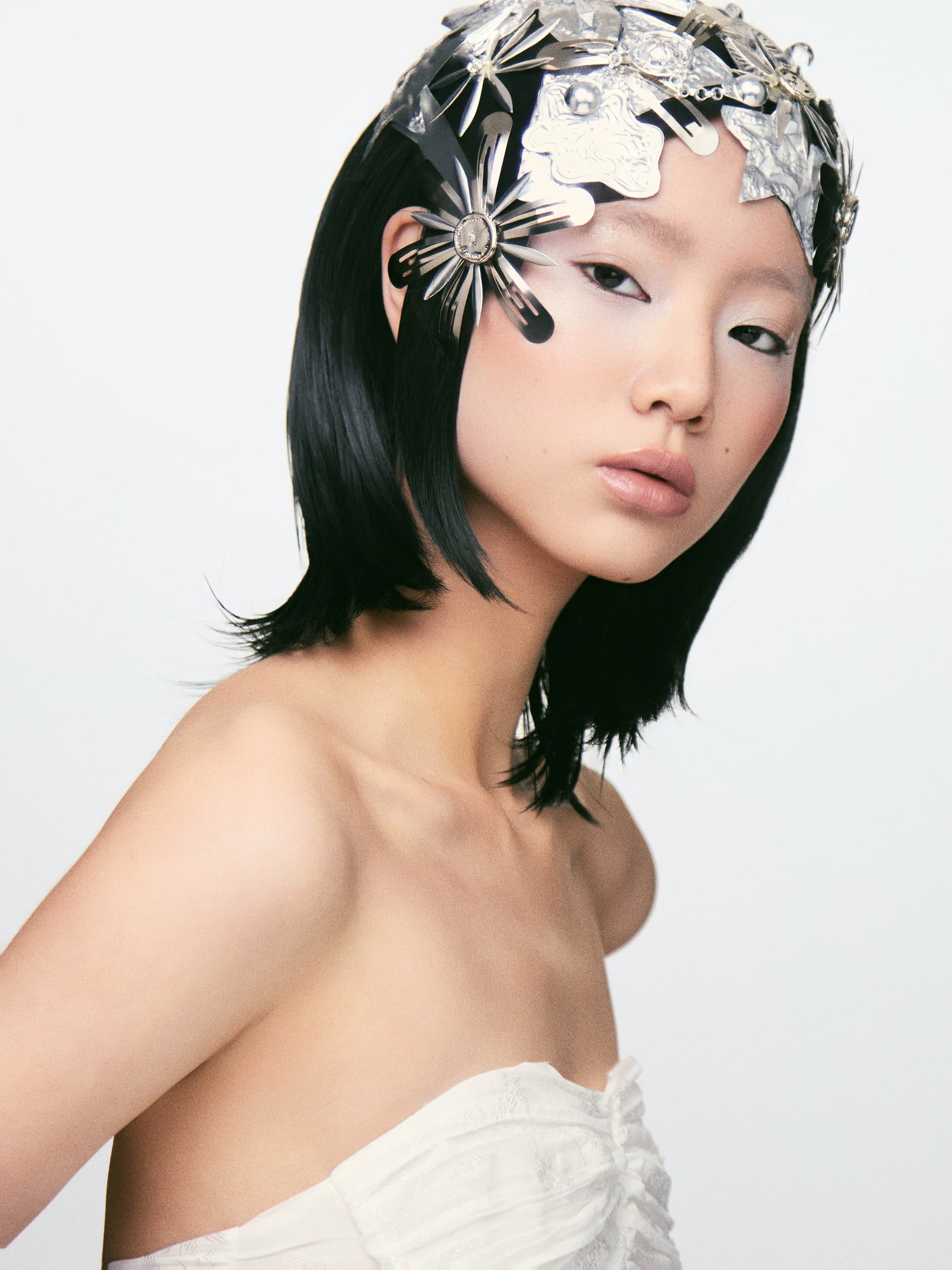 Fashion model wearing a silver headpiece and strapless dress against a neutral background.
