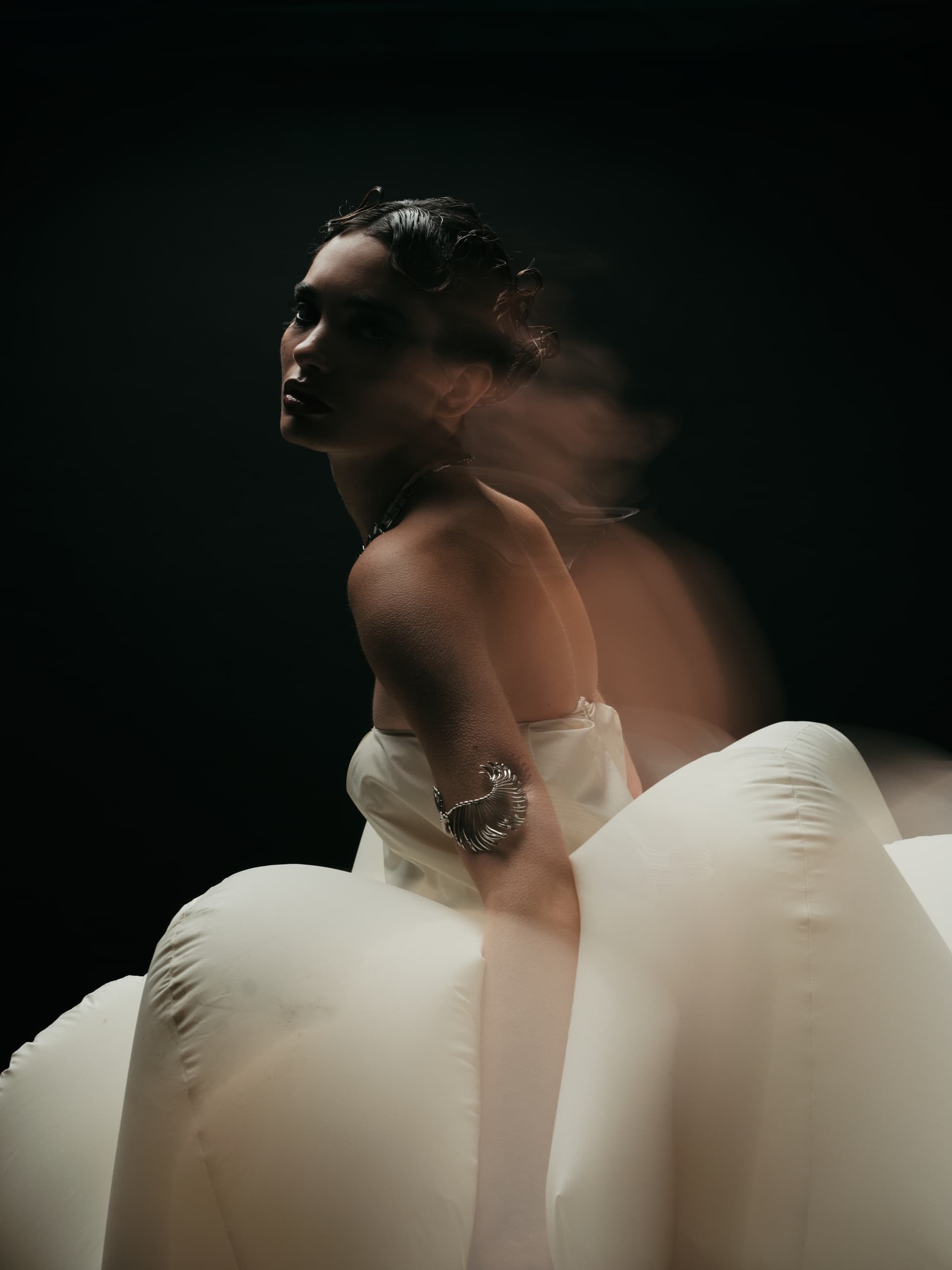 Elegant model in artistic pose, wearing a stylish gown and unique arm accessory.