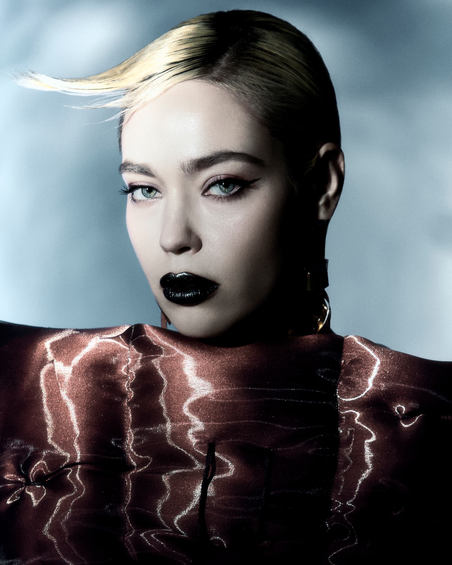 Glamorous woman with sleek hair and bold makeup wearing a stylish metallic outfit.