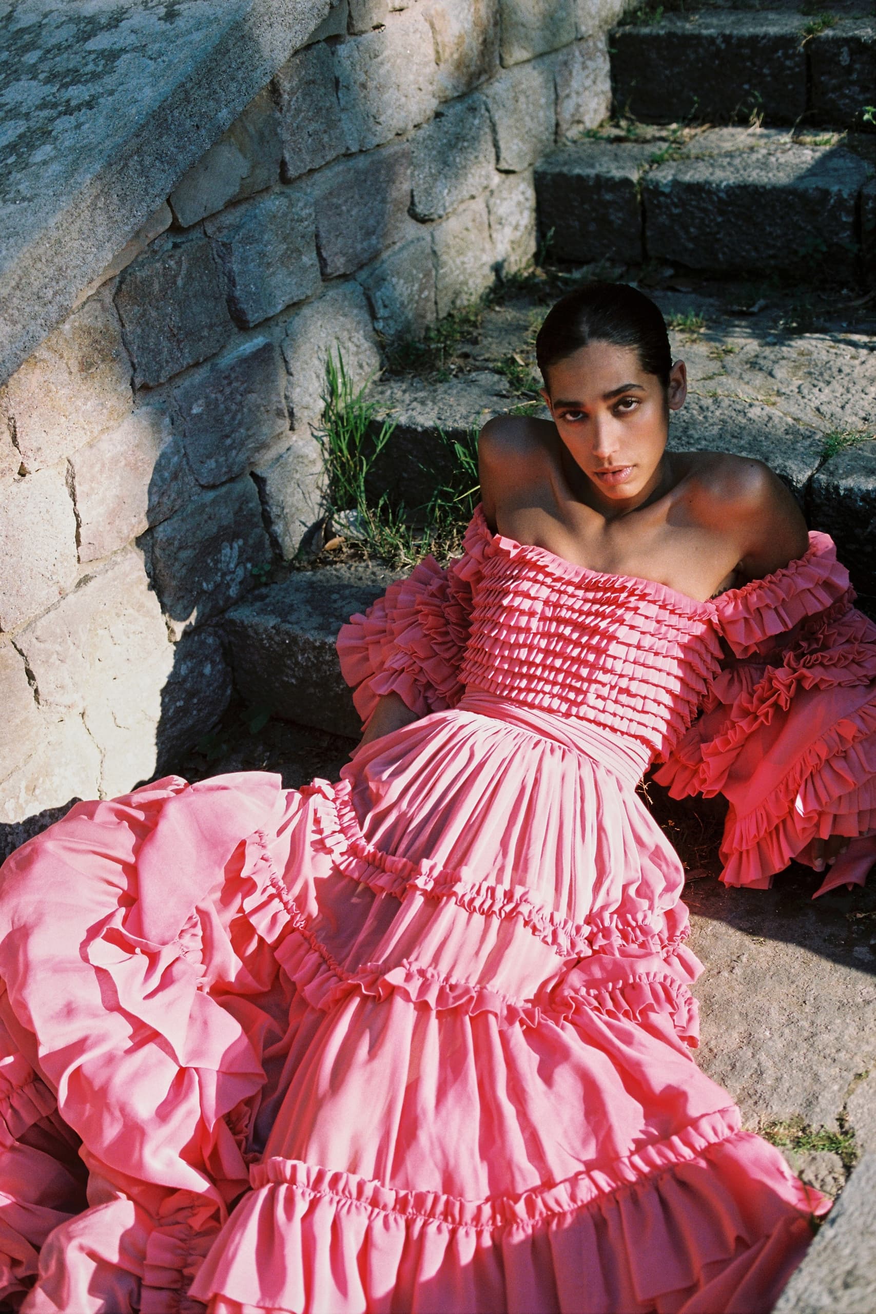 Woman in a vibrant pink ruffled dress on stone steps, exuding elegance and fashion.