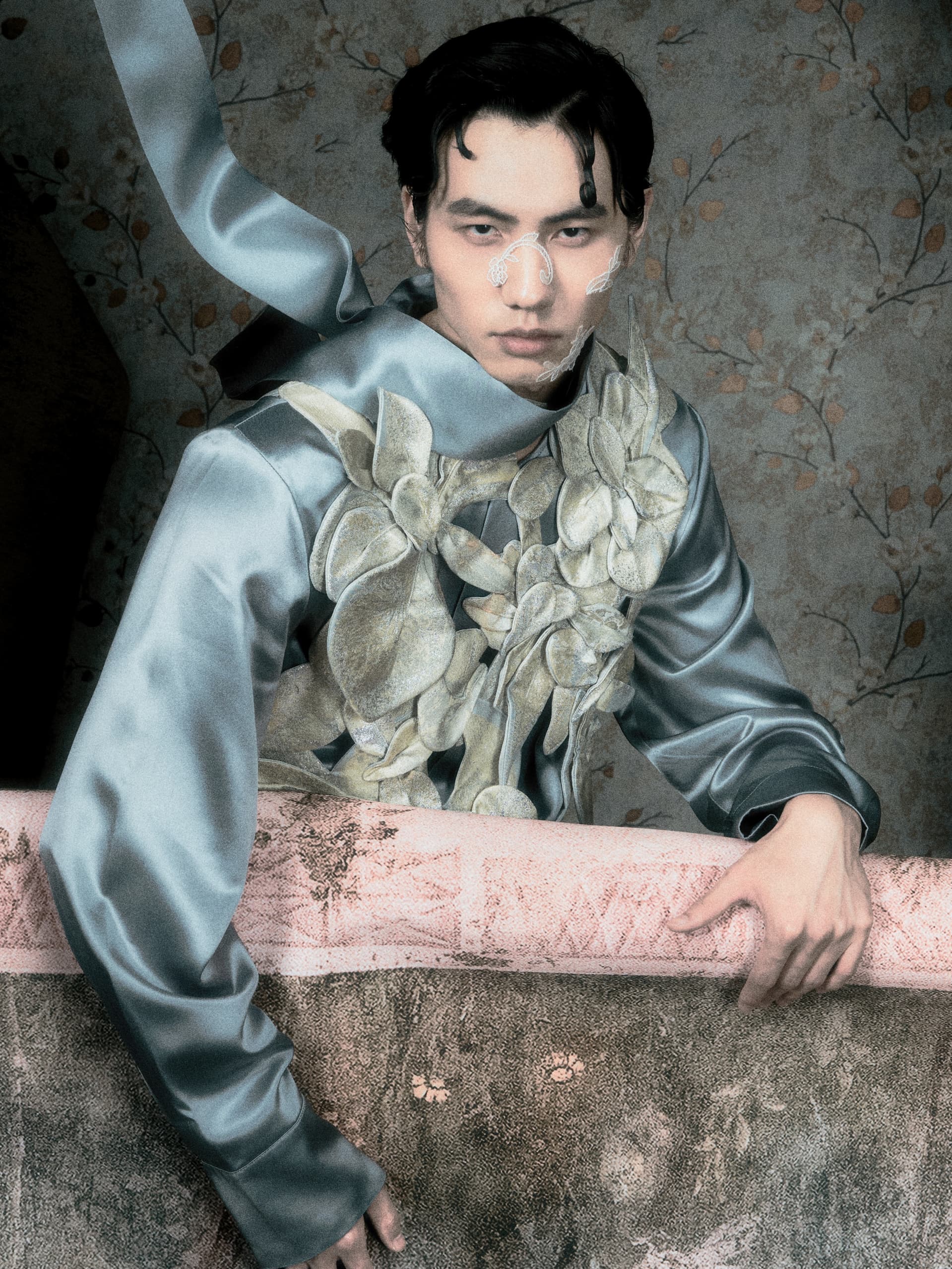 Fashion model in floral-themed silk outfit, posing against patterned wallpaper.