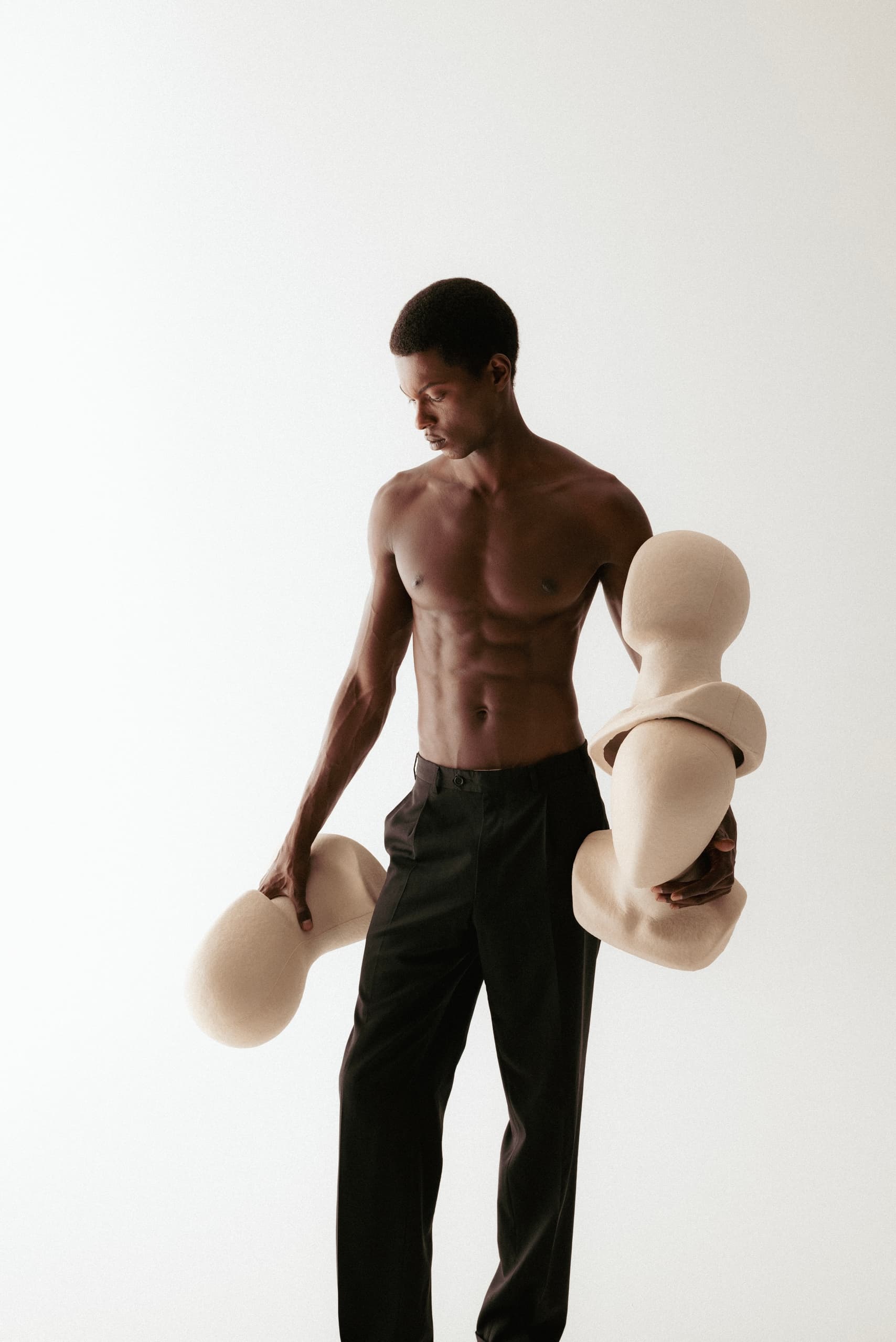 Man holding abstract sculptures, black pants, minimalistic light setting.