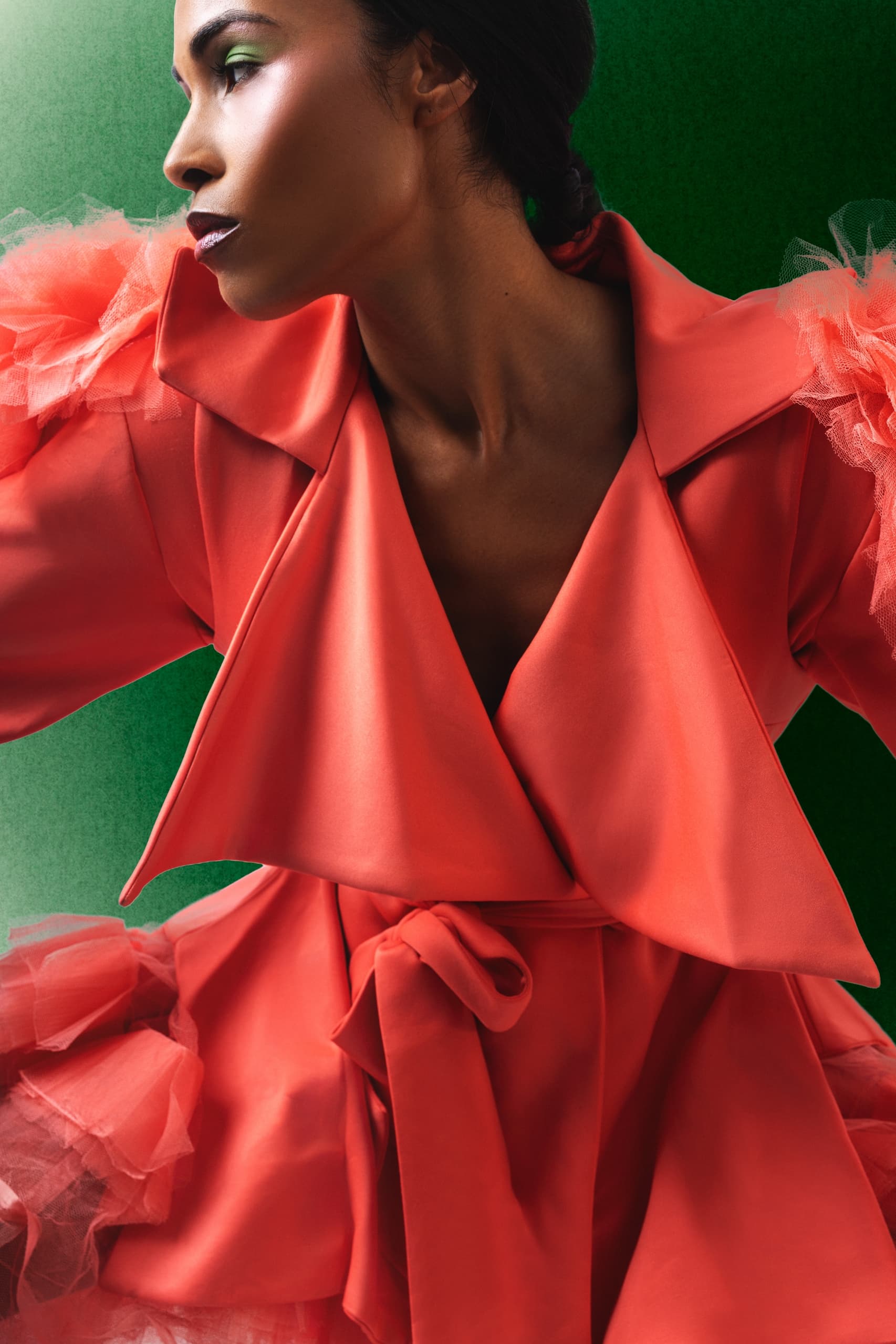 Woman in stylish red coat with ruffled sleeves, green background. Fashion portrait.