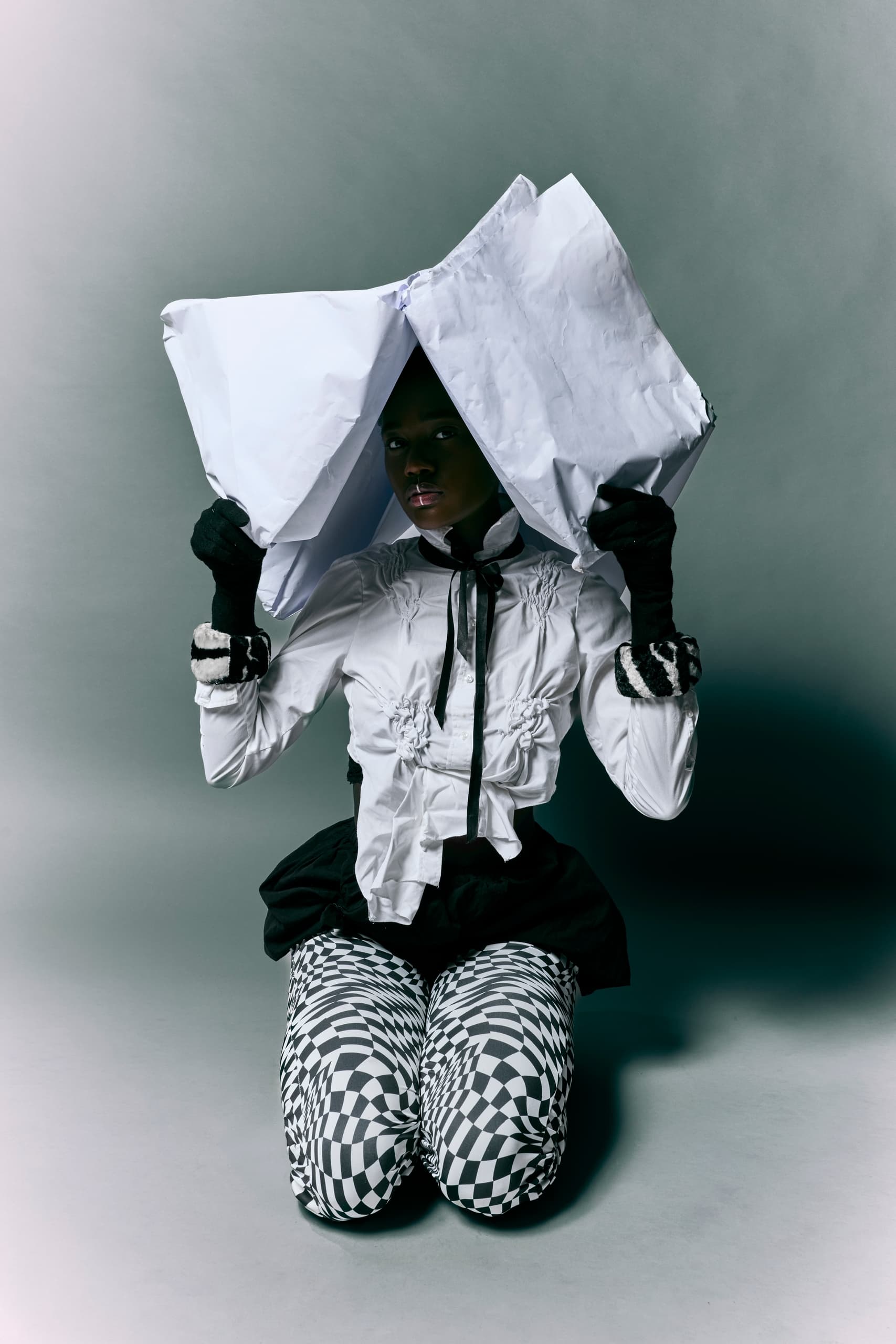 Person dressed in avant-garde fashion holding large paper in creative portrait.