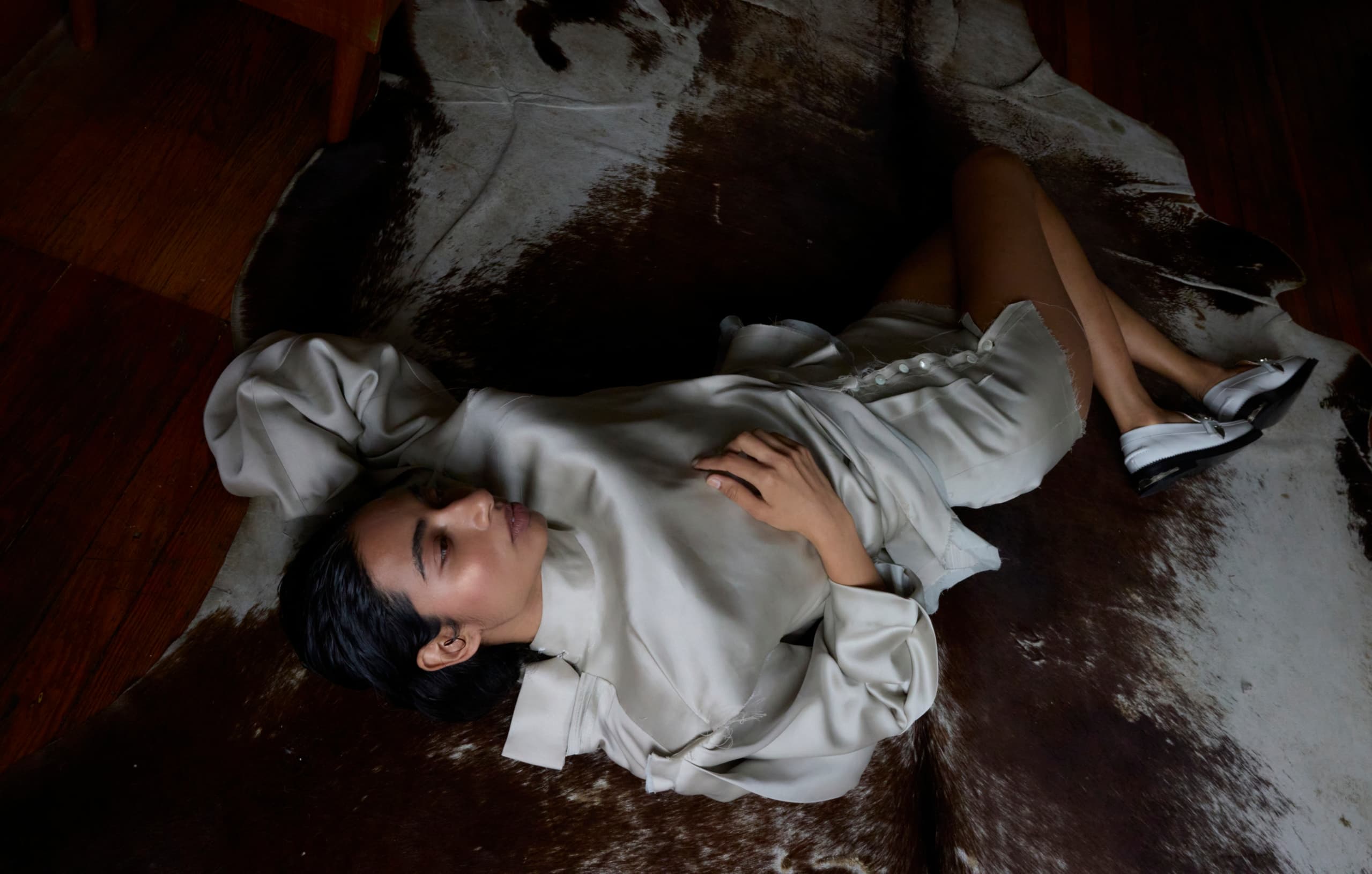 Woman in white silk outfit lying on a dark patterned rug.