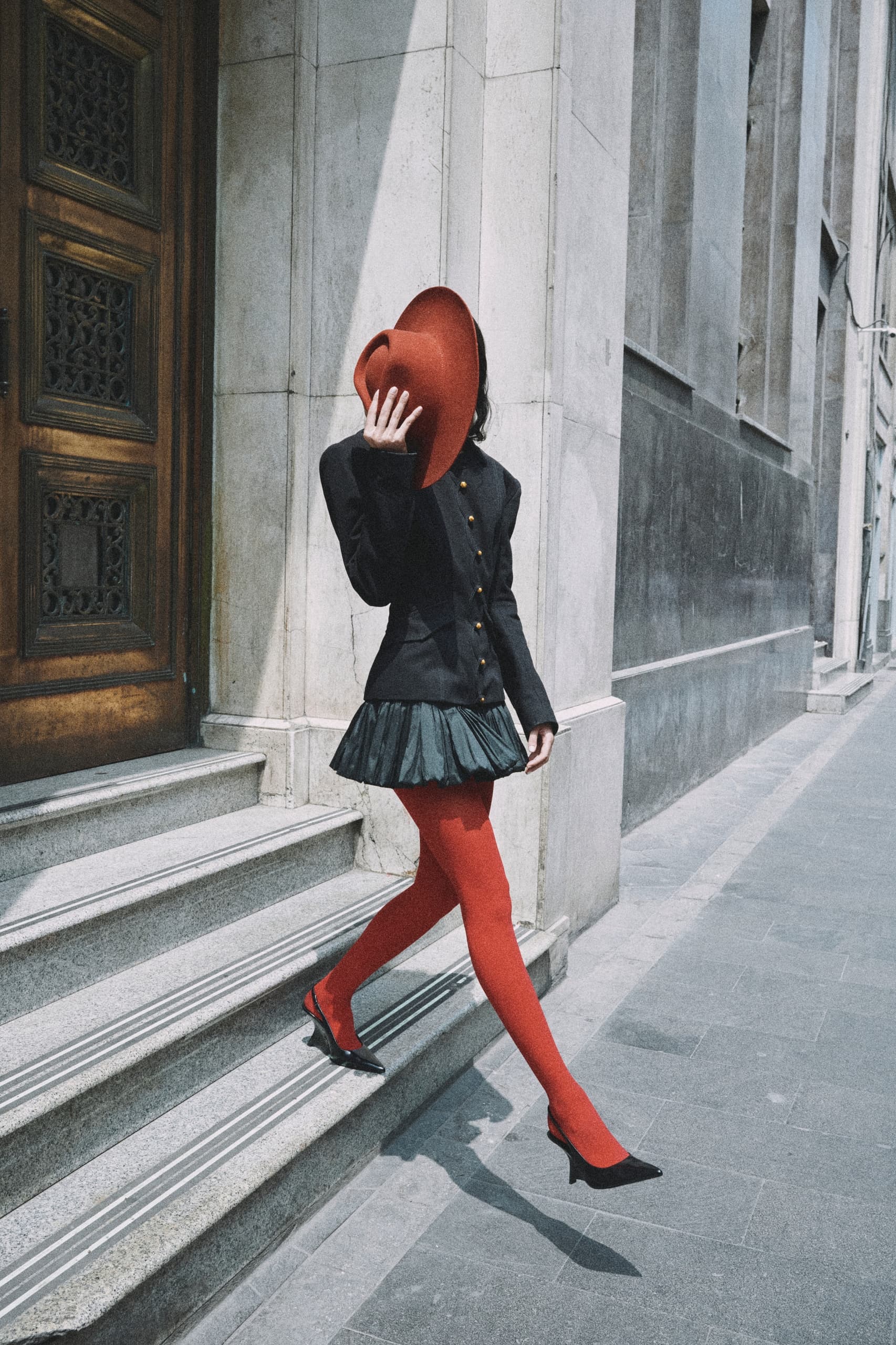 Fashionable woman in black coat and red hat walking down city steps.