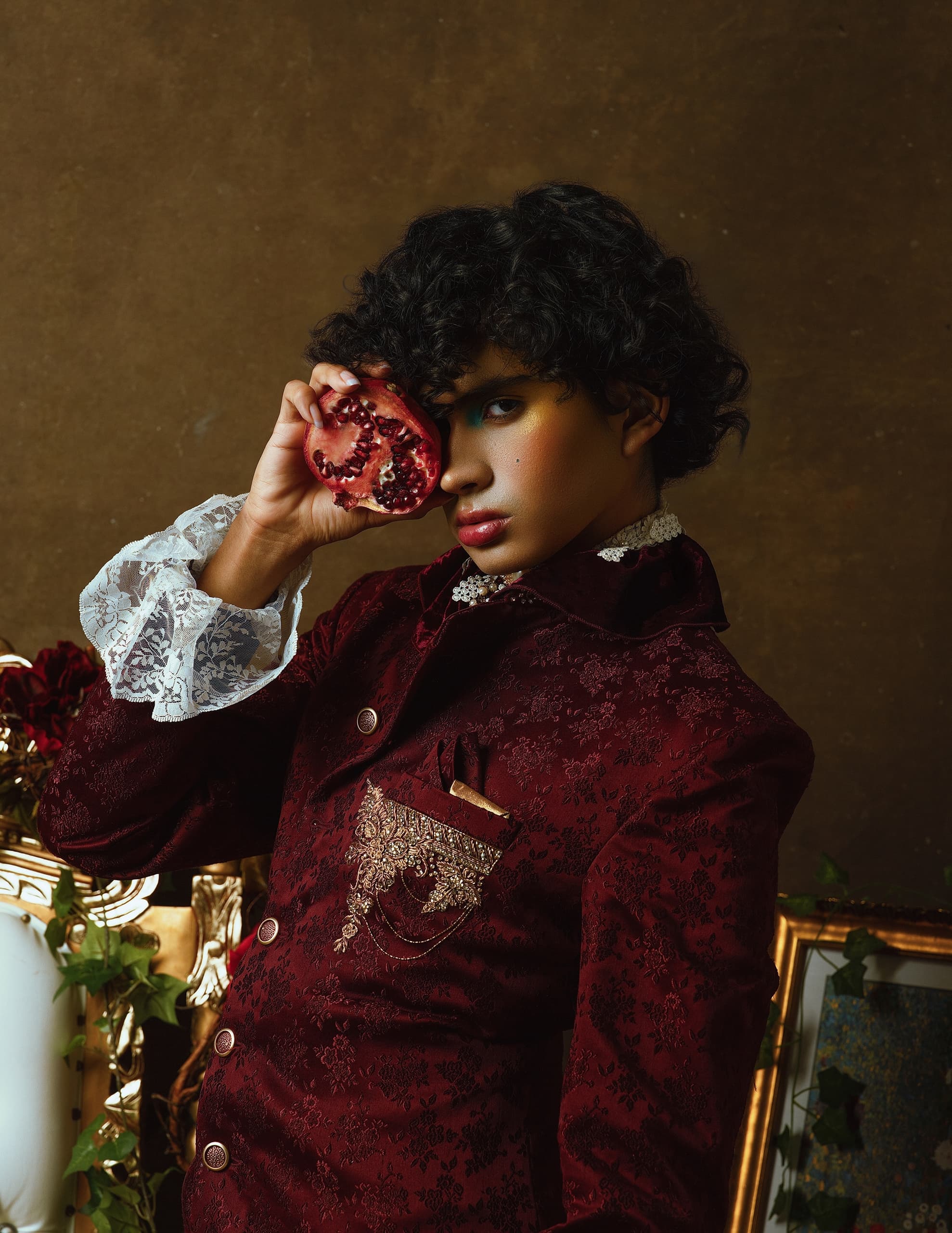 Person in ornate velvet jacket holding pomegranate, vintage aesthetic.