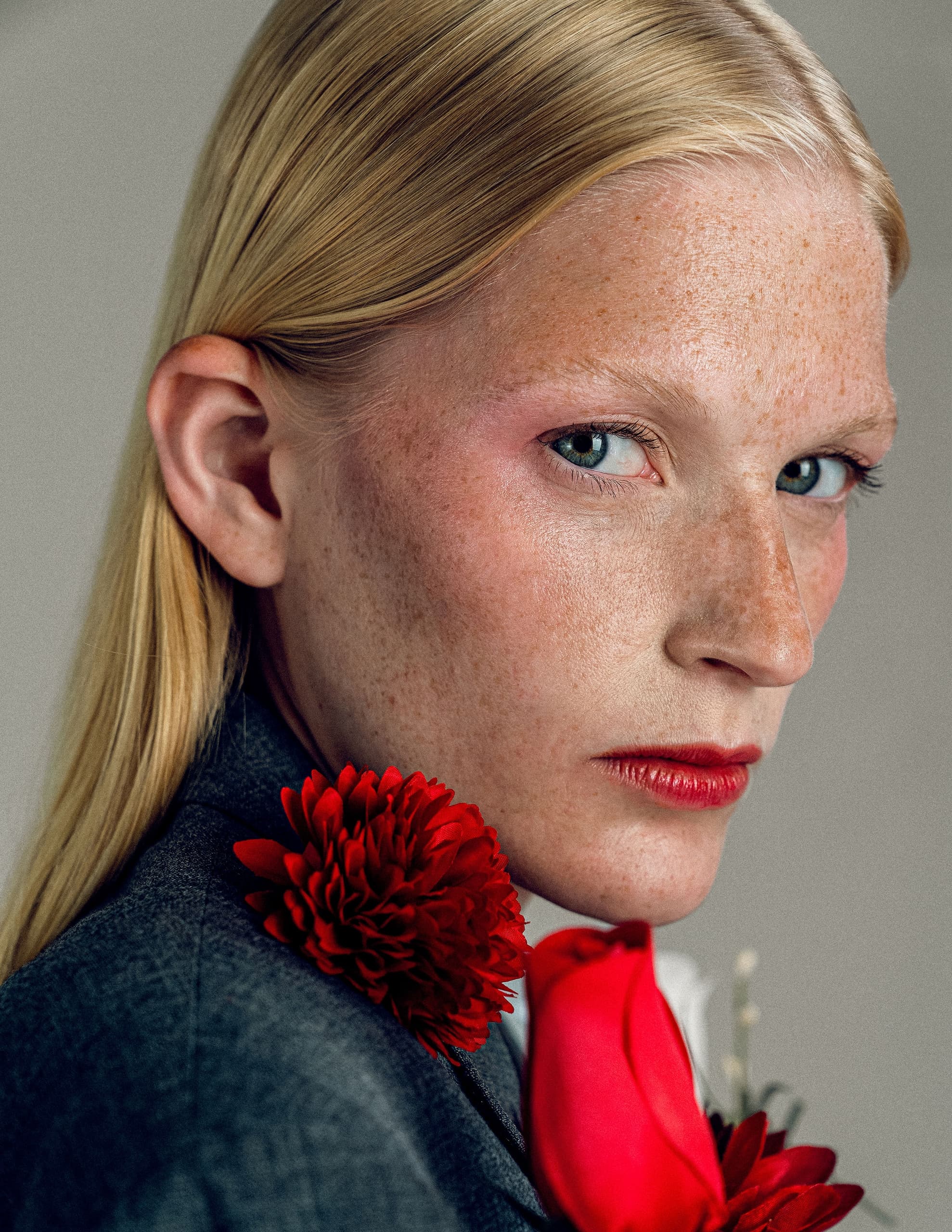 Close-up portrait with red lipstick and flowers, highlighting blonde hair and freckles.