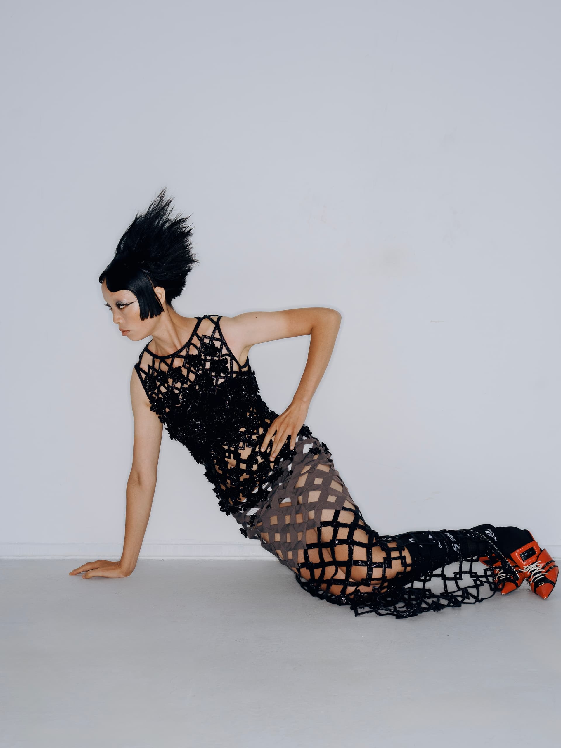 Avant-garde fashion model wearing a black lattice dress and futuristic hairstyle.