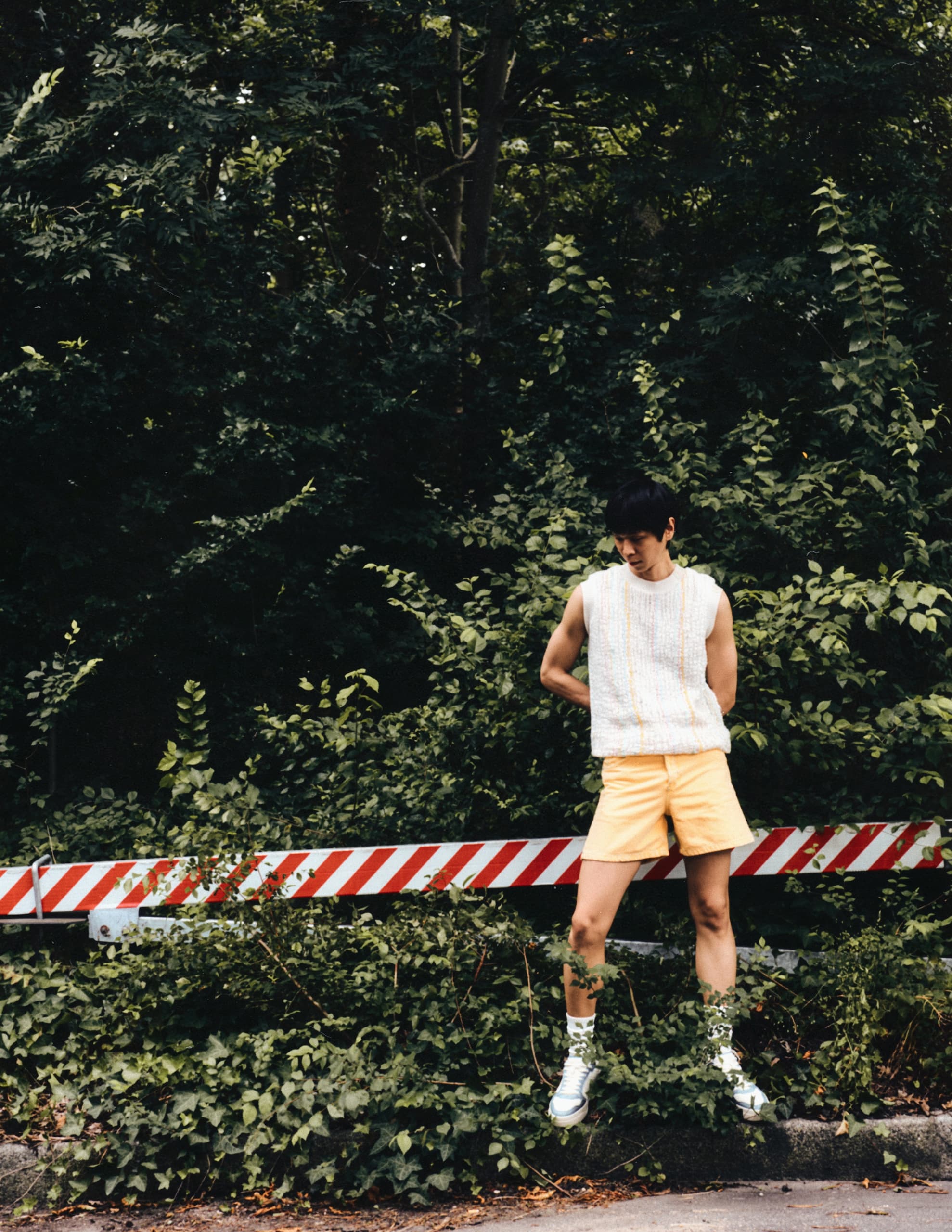 Person in yellow shorts and white top standing by striped barrier in forest.