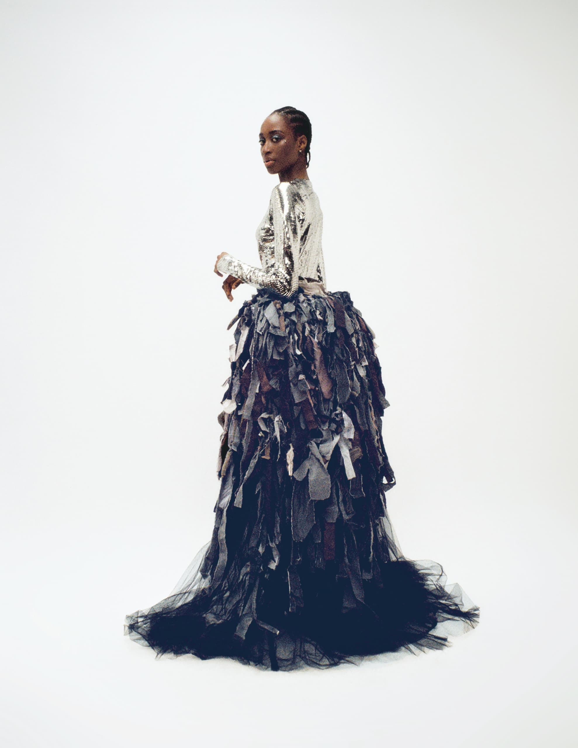 Elegant model in metallic top with textured dark gown on white background.