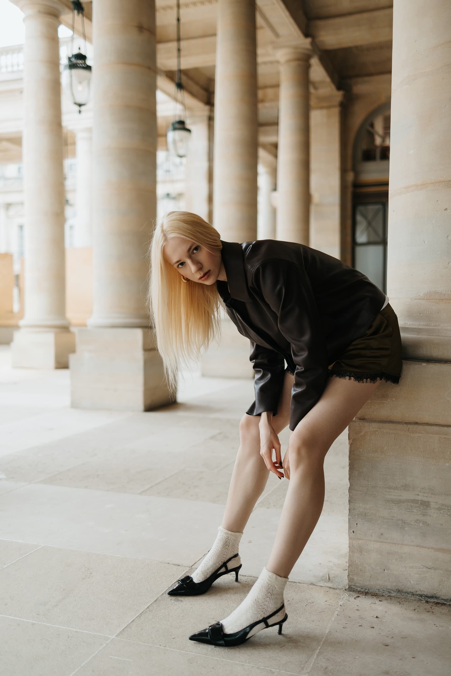 Fashionable woman in black outfit poses by stone columns.