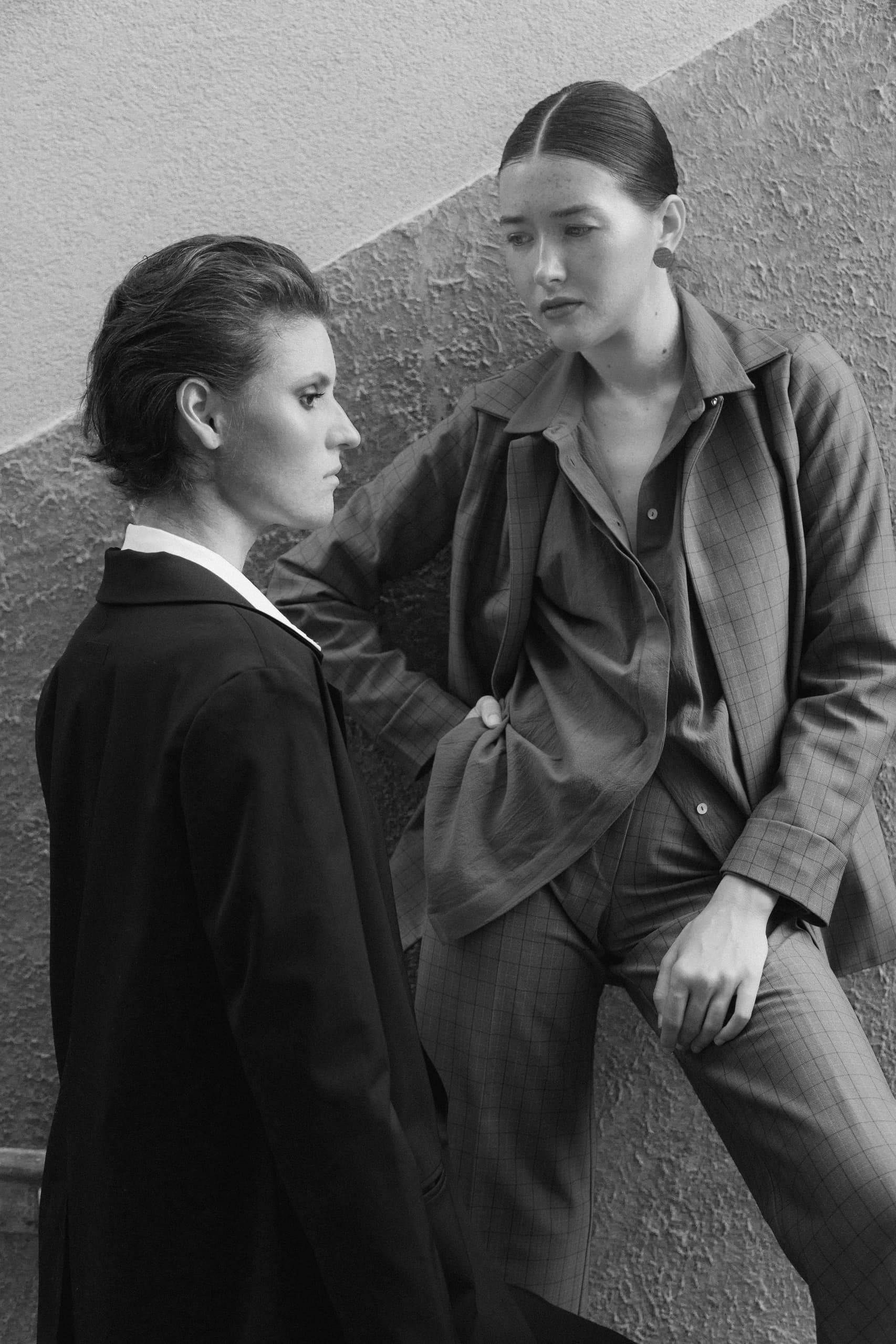Two people in stylish suits posing in a black and white photo.