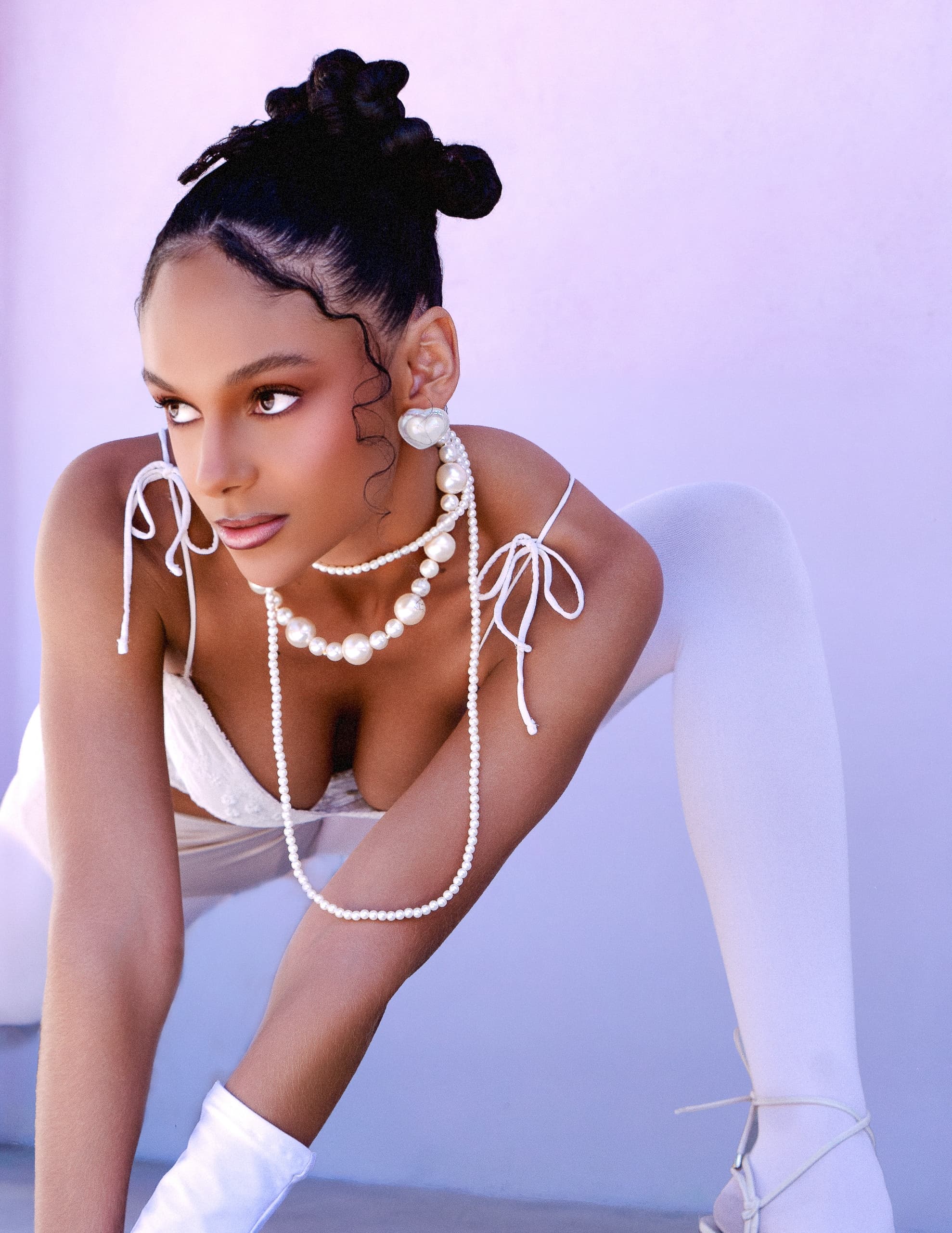 Elegant woman in pearl jewelry poses against a soft purple backdrop.