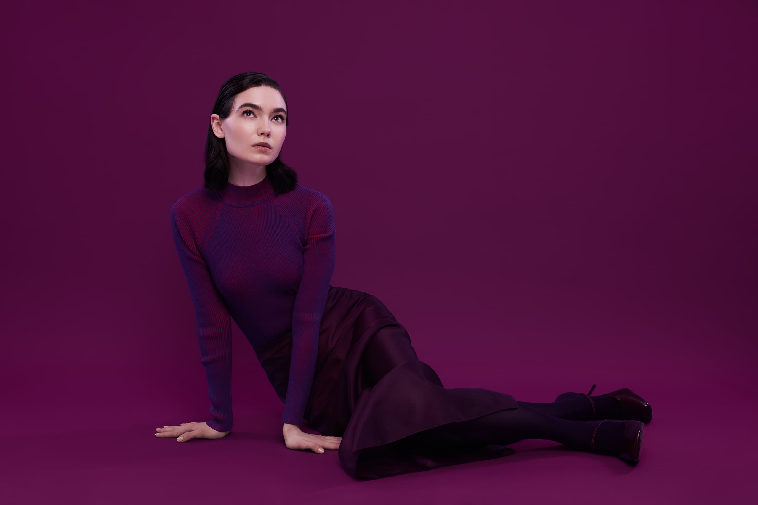 Woman in purple outfit sitting against a deep purple background.