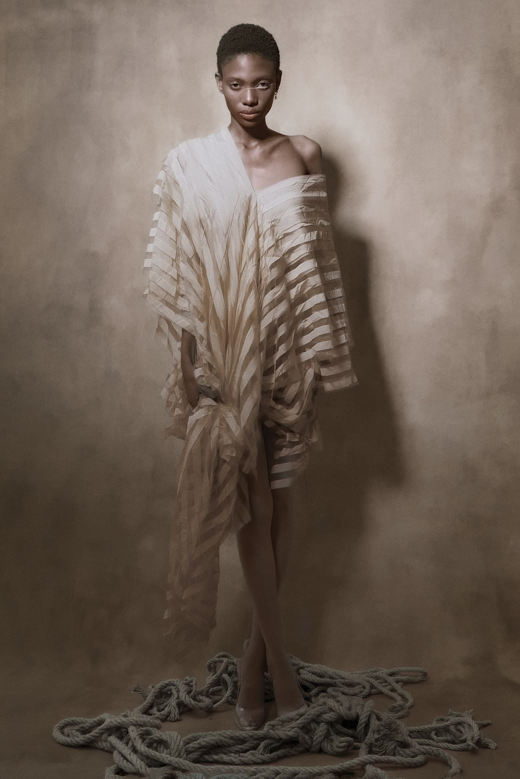 Elegant model in sheer, striped gown standing on coiled ropes.