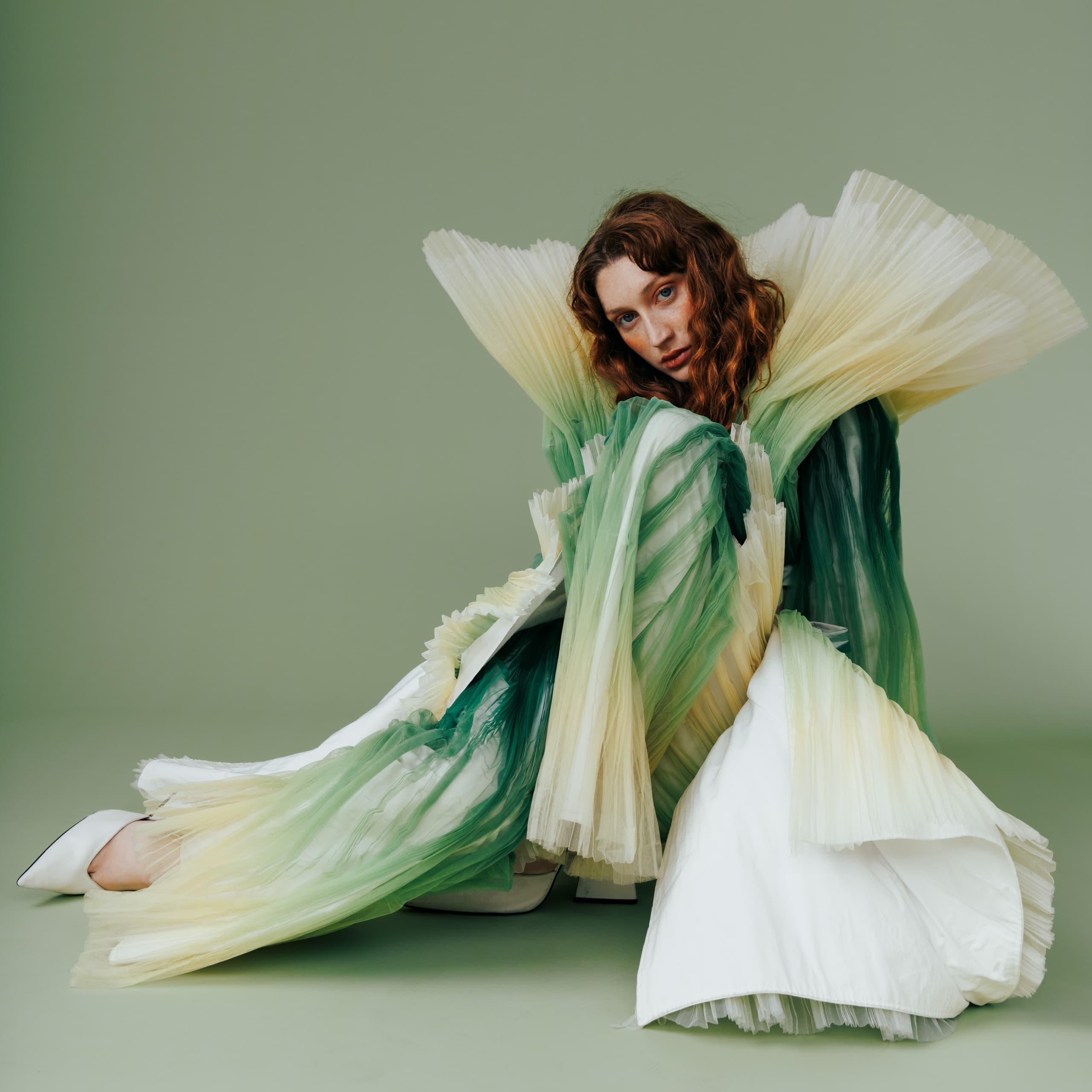 Avant-garde fashion outfit with pleated green and white fabric on green background.