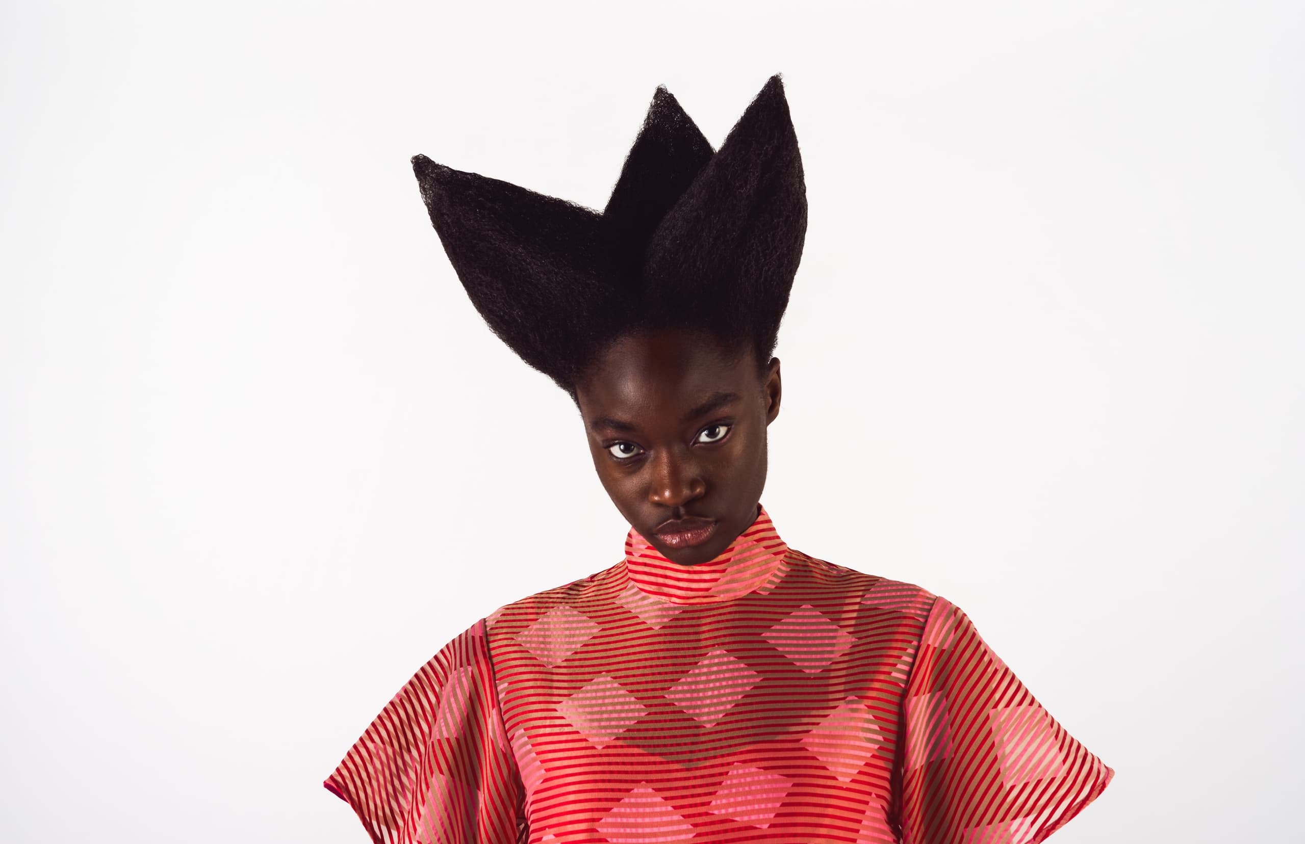 Model in geometric red outfit with sculpted hair and a bold look.