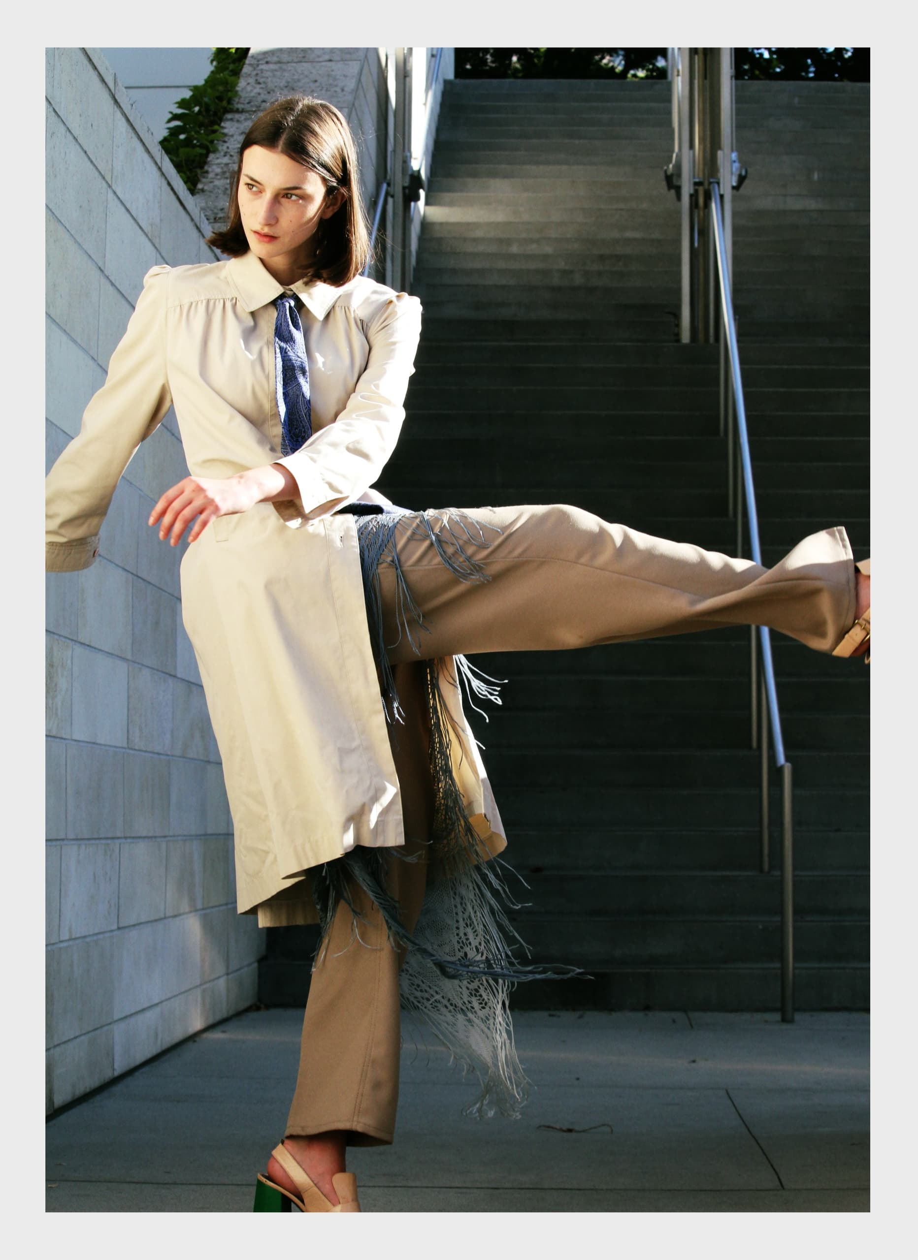 Fashionable individual posing in stylish beige trench and pants on urban staircase.