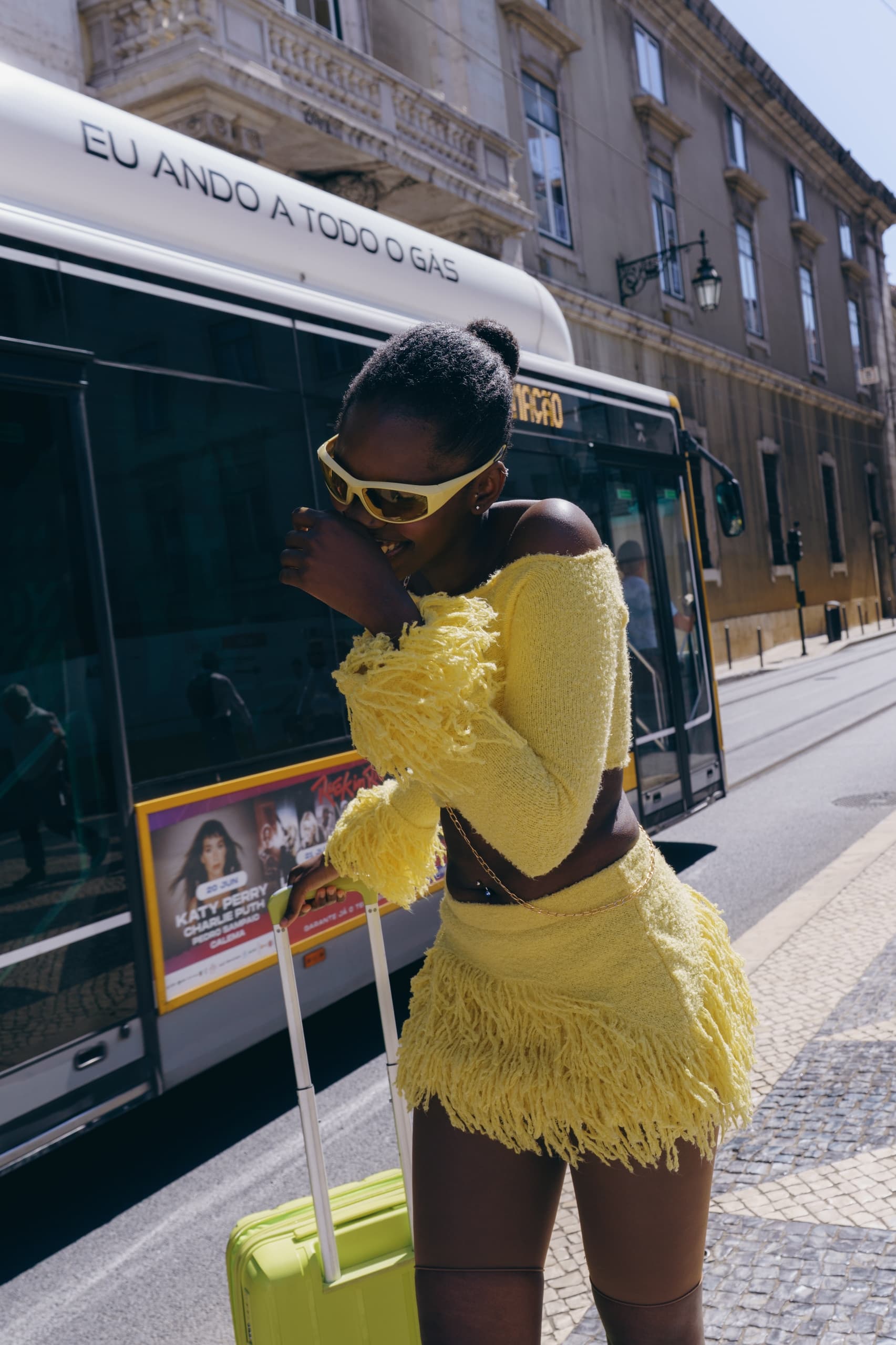 Fashionable woman in yellow outfit with suitcase near city bus.