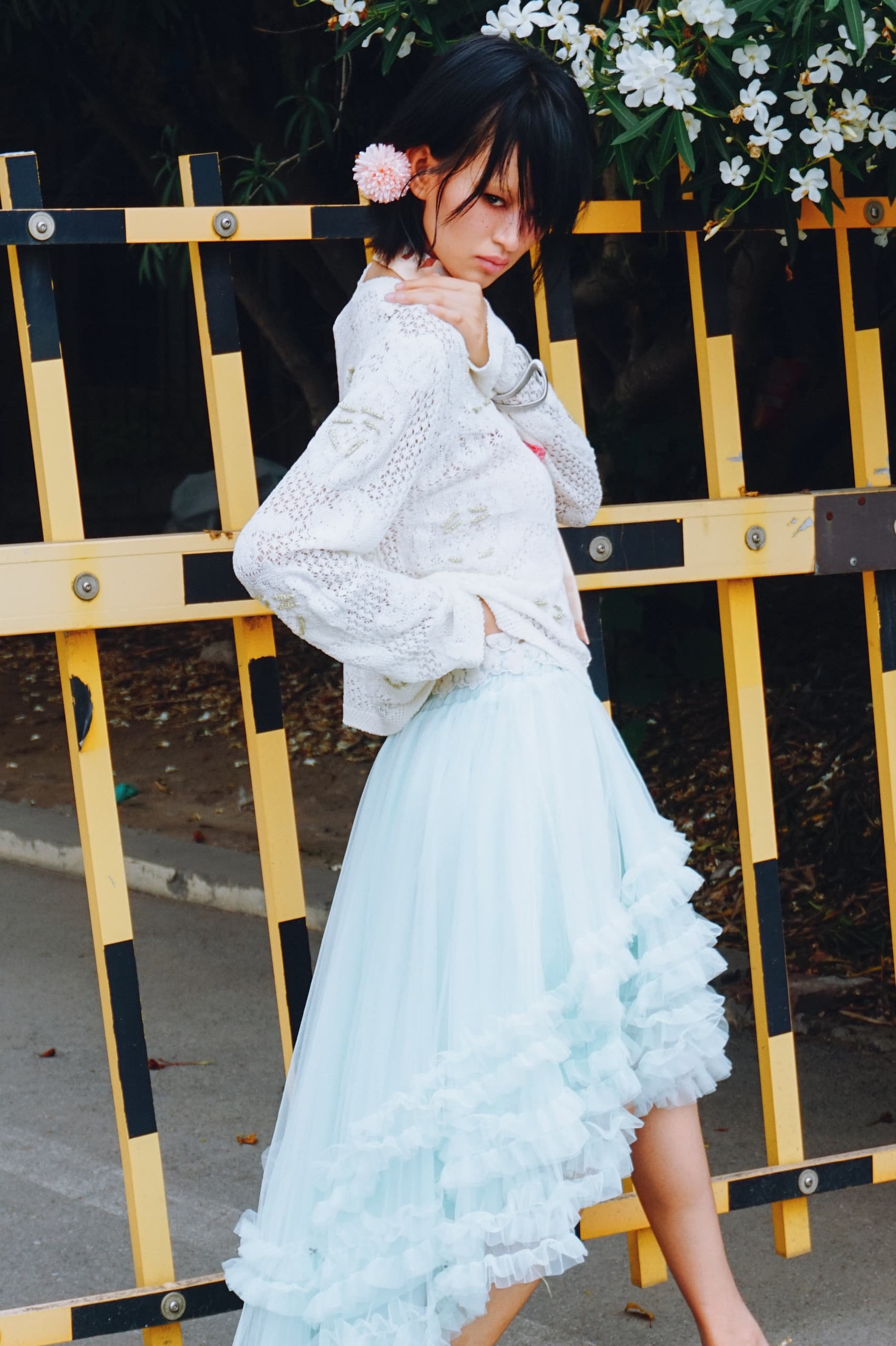 Fashionable woman in a frilly blue skirt posing outdoors near flowers.