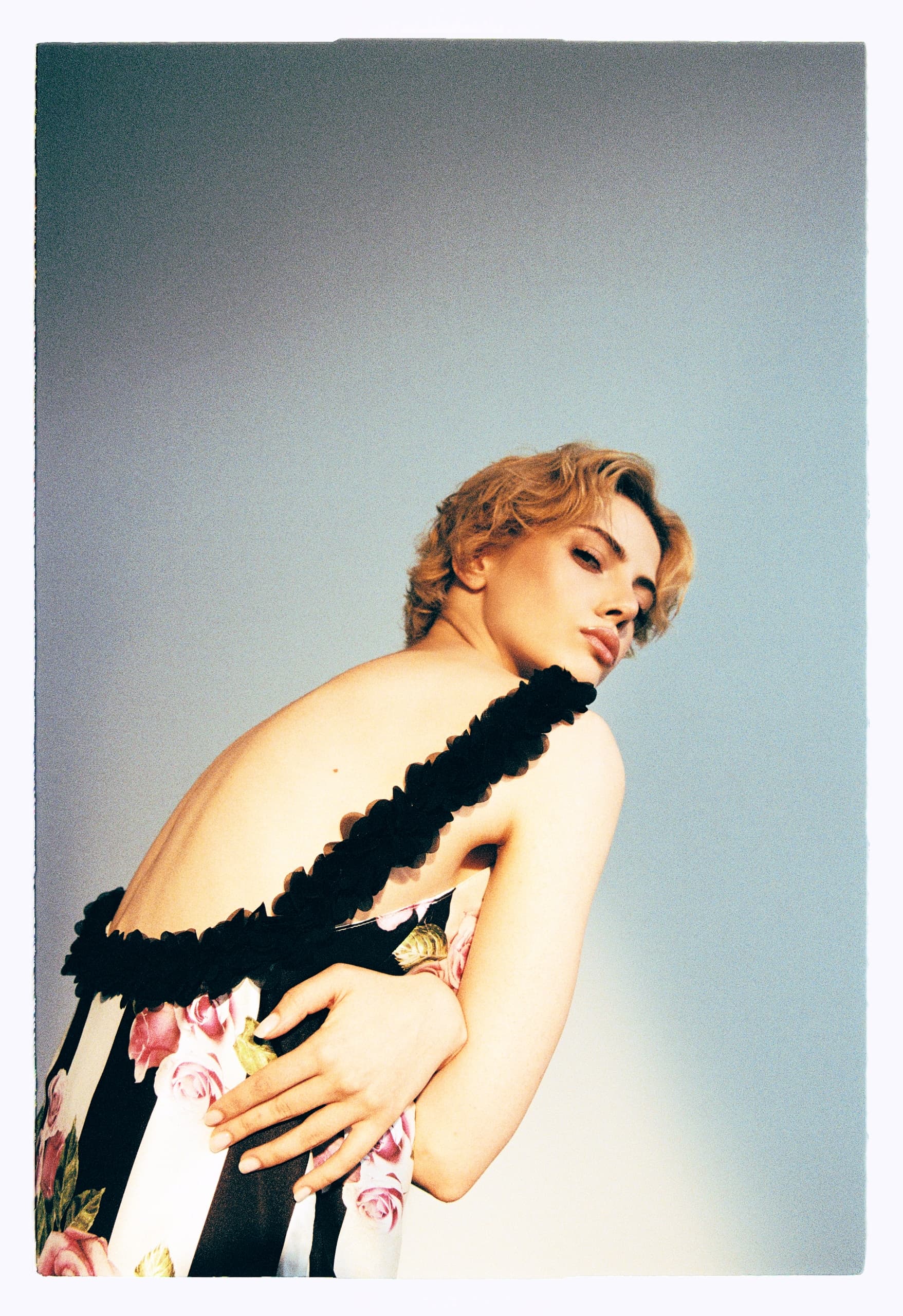 Person in a floral striped dress posing with a confident, artistic style.