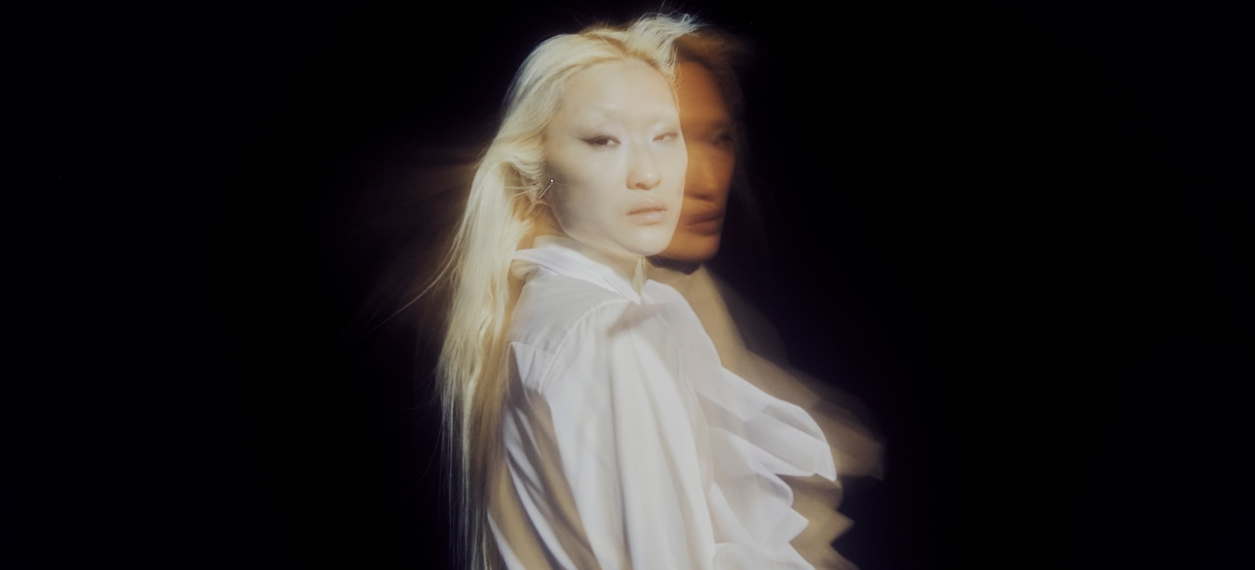 Mysterious double exposure portrait with flowing blonde hair on dark background.