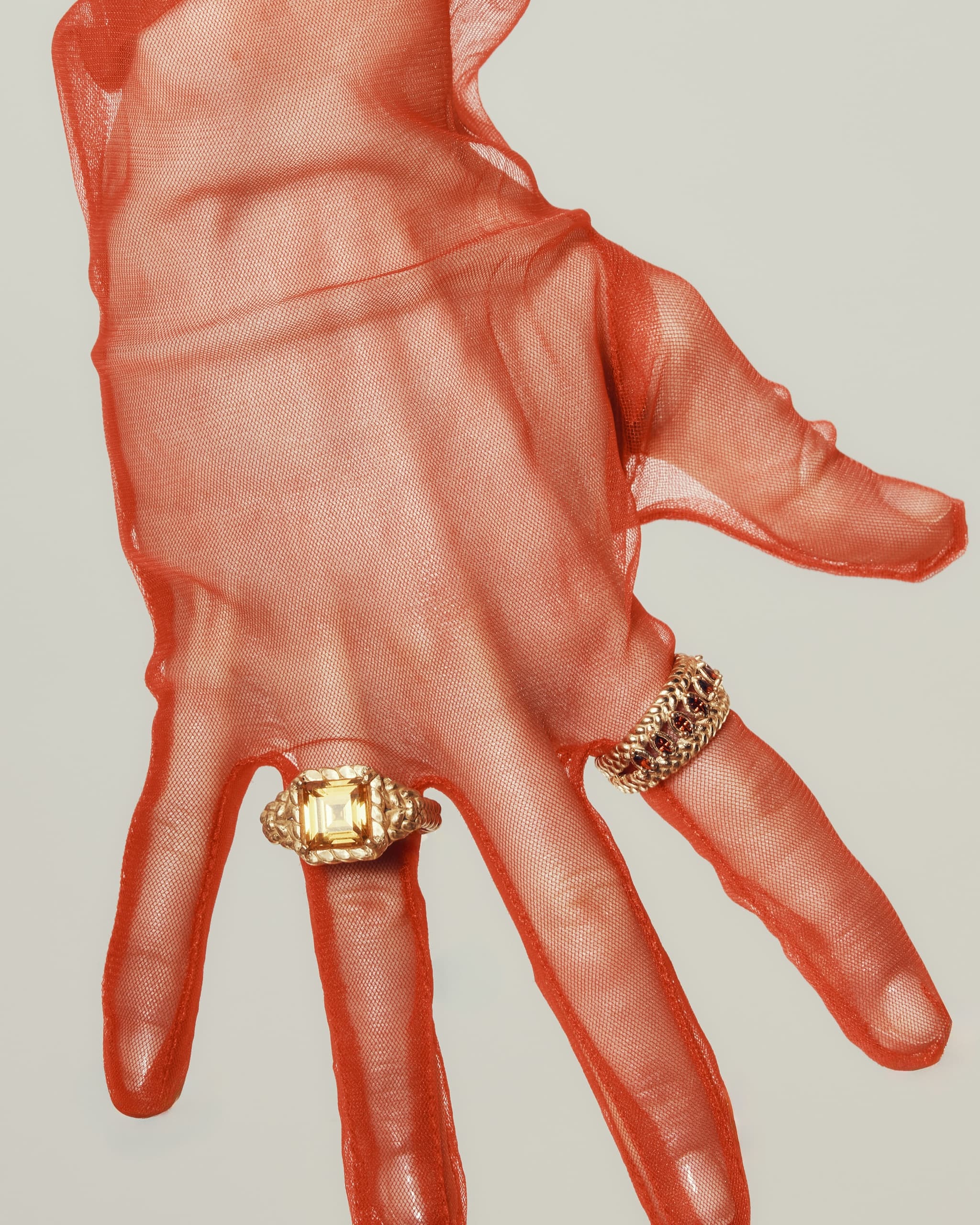 Elegant gold rings on gloved hand with sheer red fabric.
