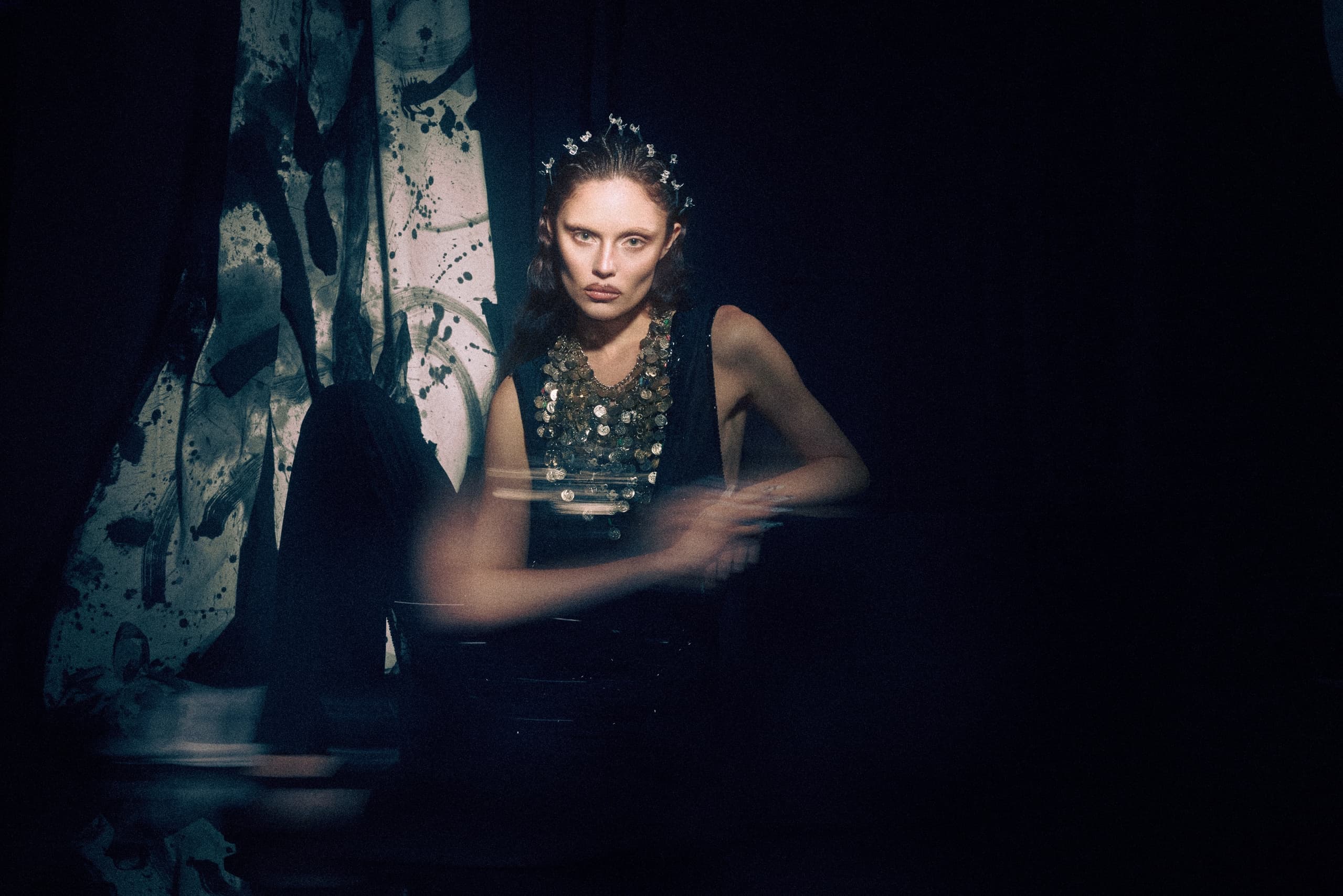 Woman posing in artistic lighting with metallic dress and dark setting.