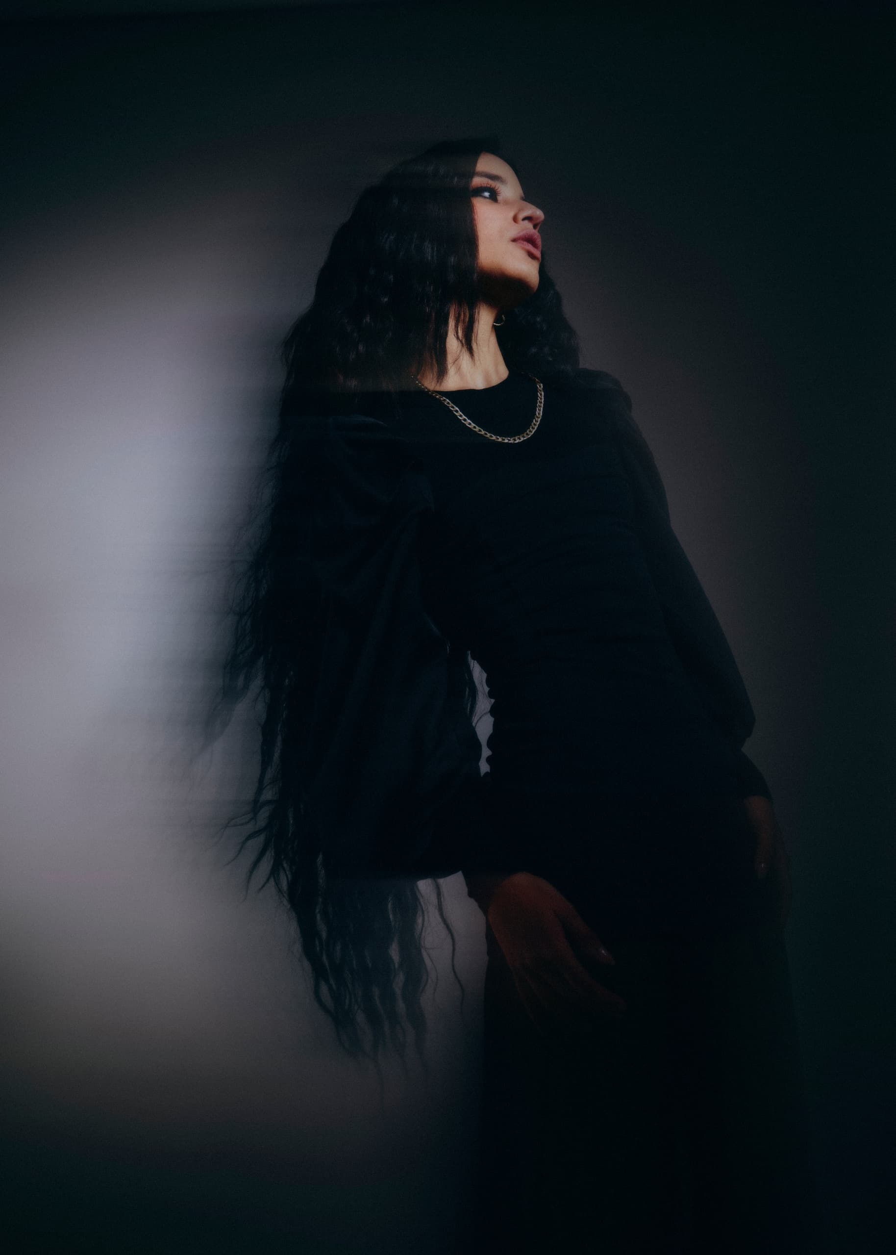 Mysterious woman in black with long hair, standing in dim lighting.