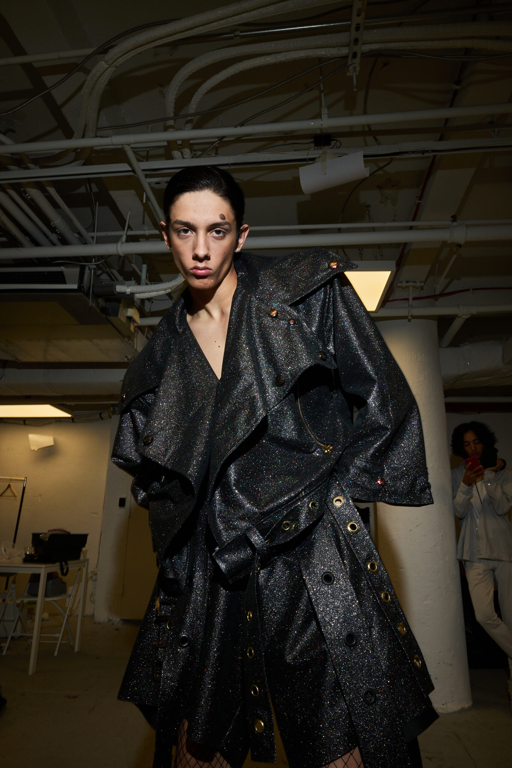 Model in sparkly dark outfit backstage at fashion show.